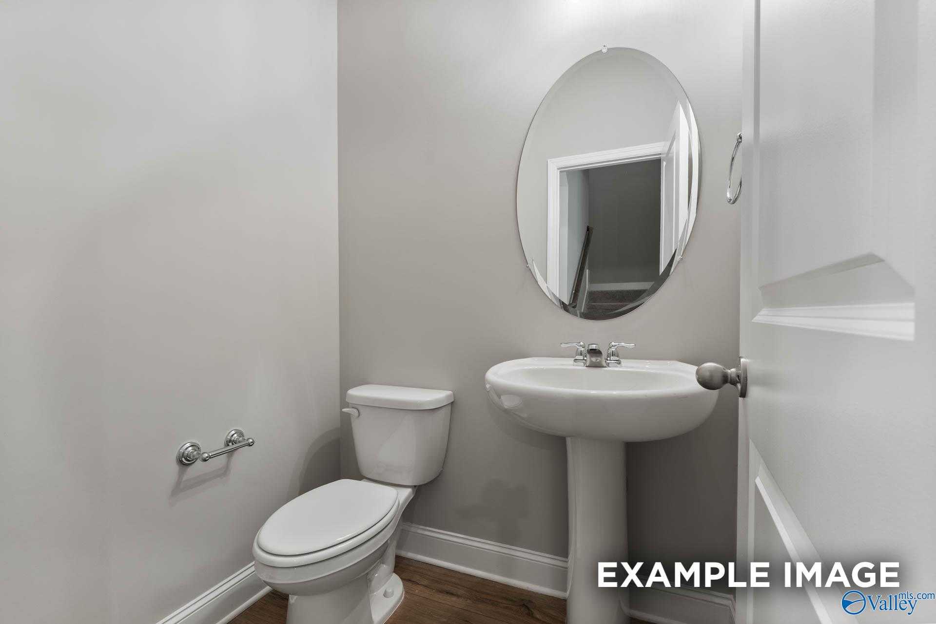 Modern powder room featuring pedestal sink, oval mirror, and white toilet in Davidson Homes The Rockford D, Hazel Green, AL