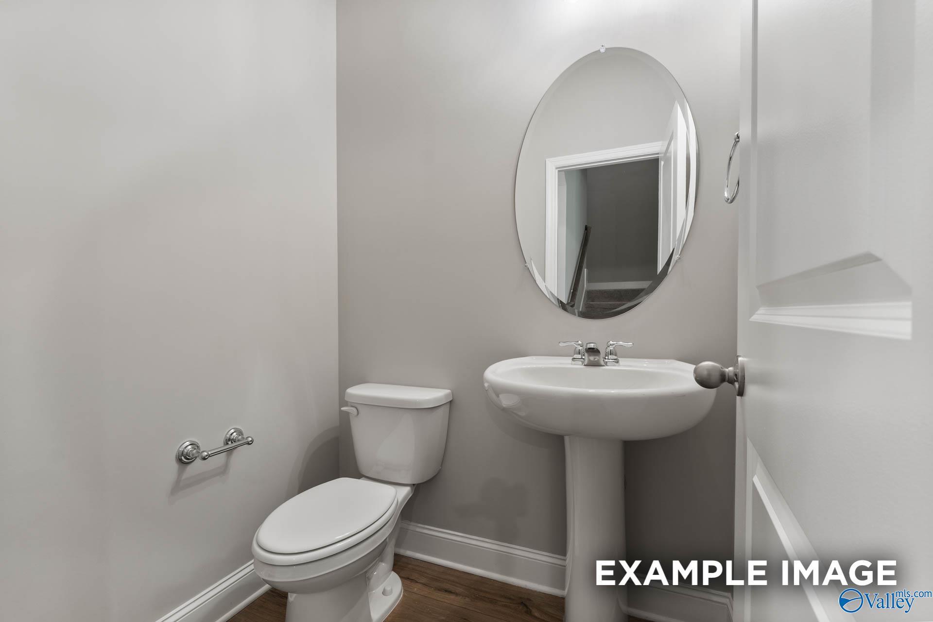 Bright powder room with white pedestal sink, oval mirror, and toilet in Davidson Homes The Rockford with Bonus, Madison, Alabama