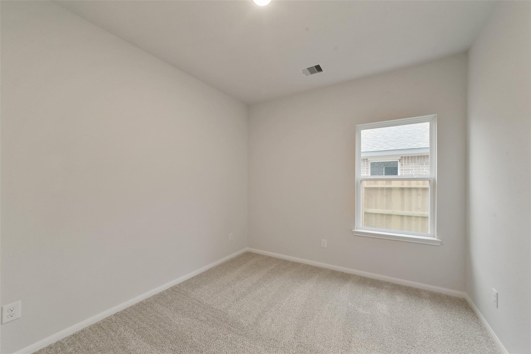 Empty secondary bedroom with beige walls, berber carpet, and window overlooking fenced backyard in Davidson Homes The San Marcos E, Beasley, TX