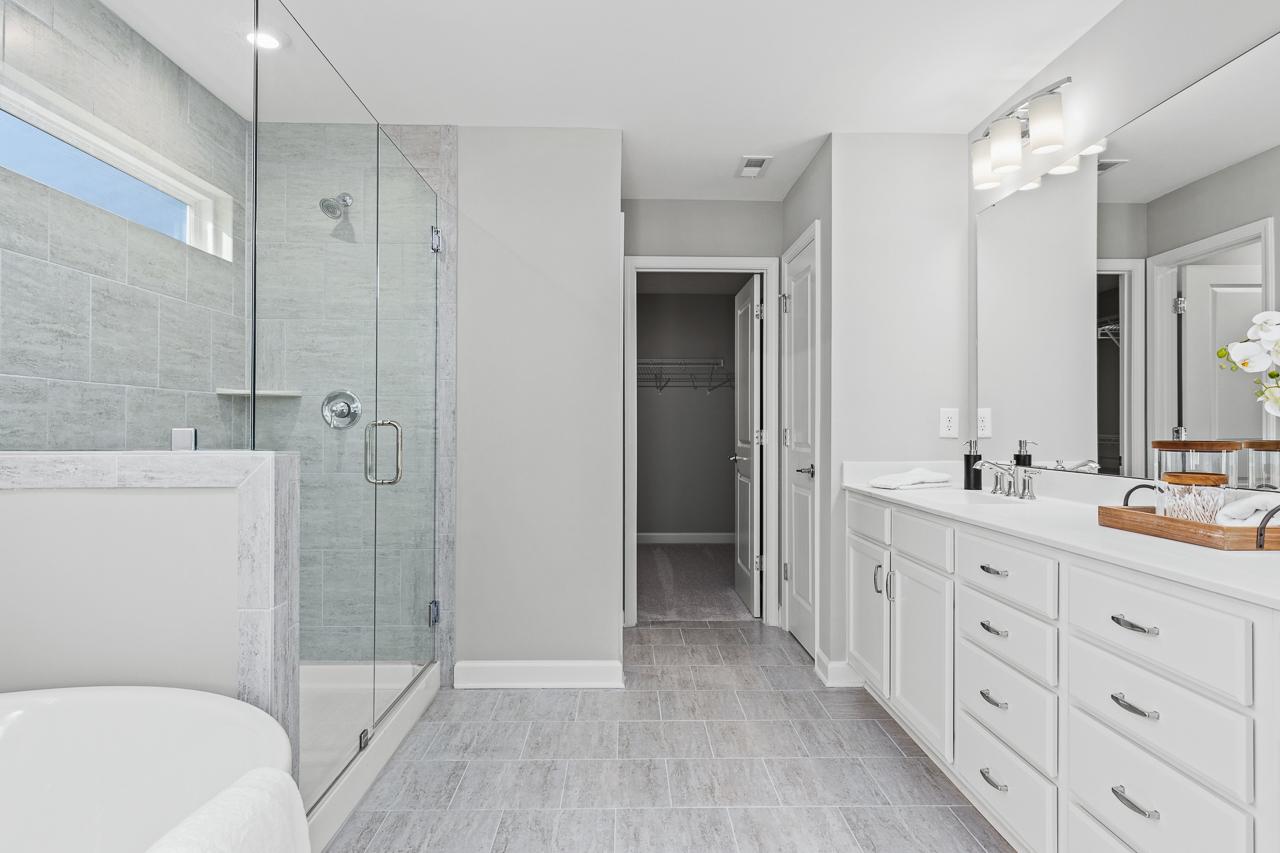 Modern master bathroom in The Hemlock A featuring a glass-enclosed shower, dual vanity, and spacious walk-in closet.