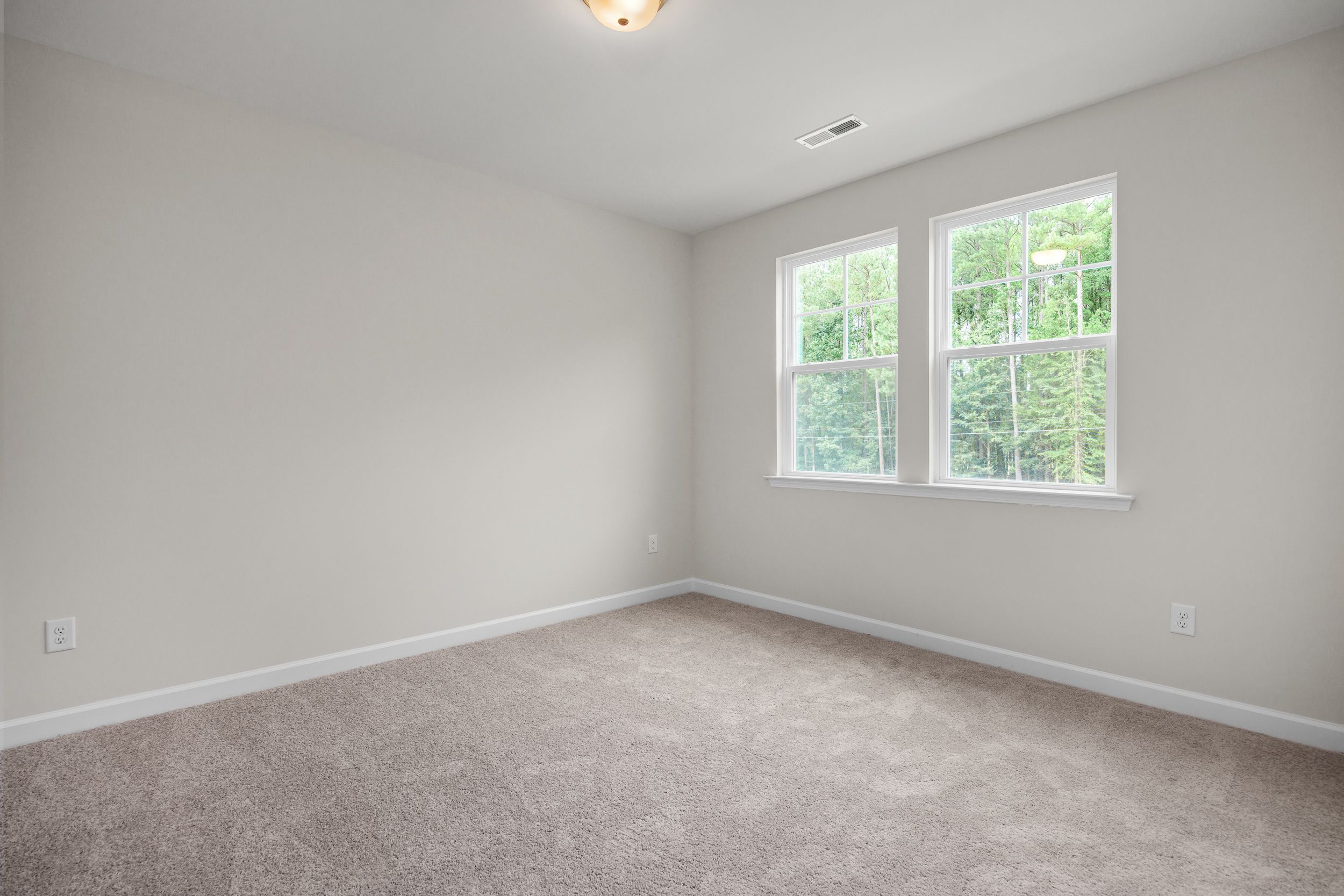 Spacious empty bedroom in The Aspen by Davidson Homes with neutral walls, large double windows, carpet flooring, and soft lighting