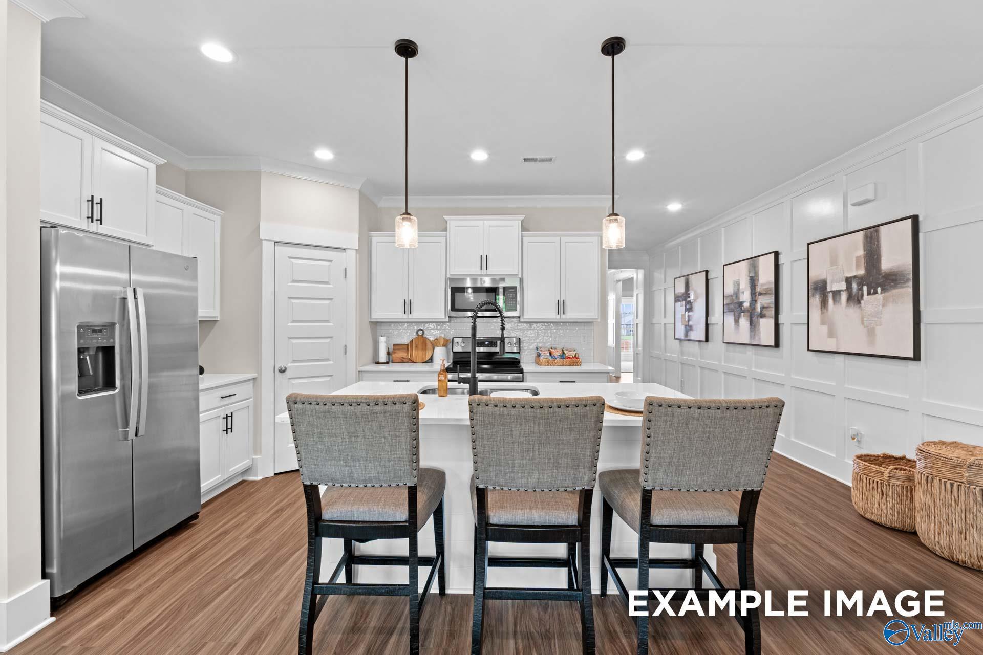 Modern open-concept kitchen featuring large island, stainless steel fridge, white cabinets, and pendant lights in The Daphne F floor plan, Berry Cove, AL