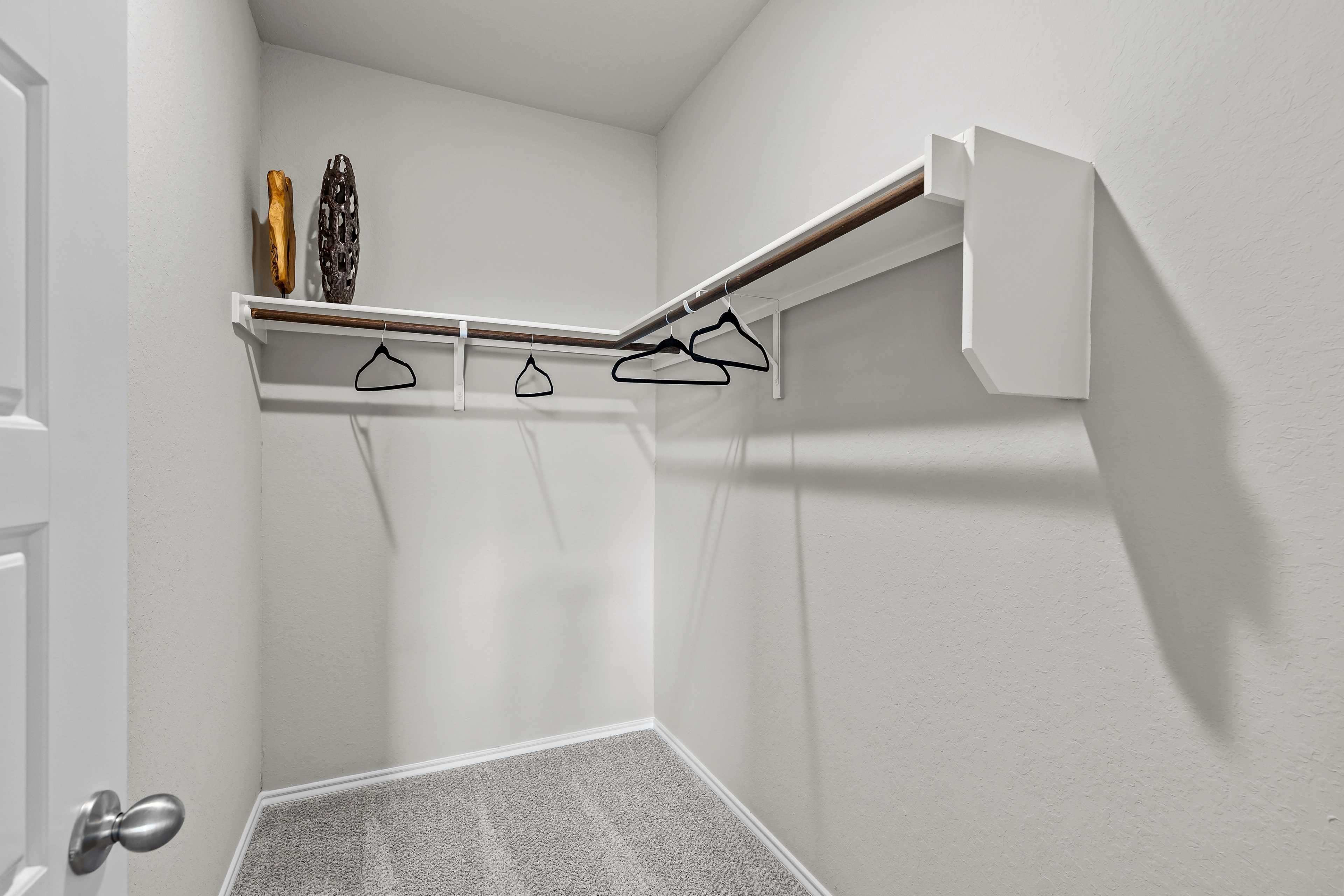 Spacious walk-in closet in The Sabine C master suite featuring built-in shelves, hanging rods, white walls, and orange vase accent