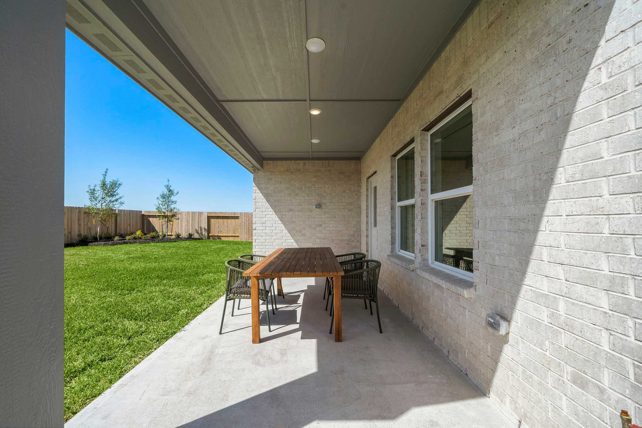 Covered patio with teak dining table and wicker chairs at River Ranch Meadows in Dayton TX by Davidson Homes