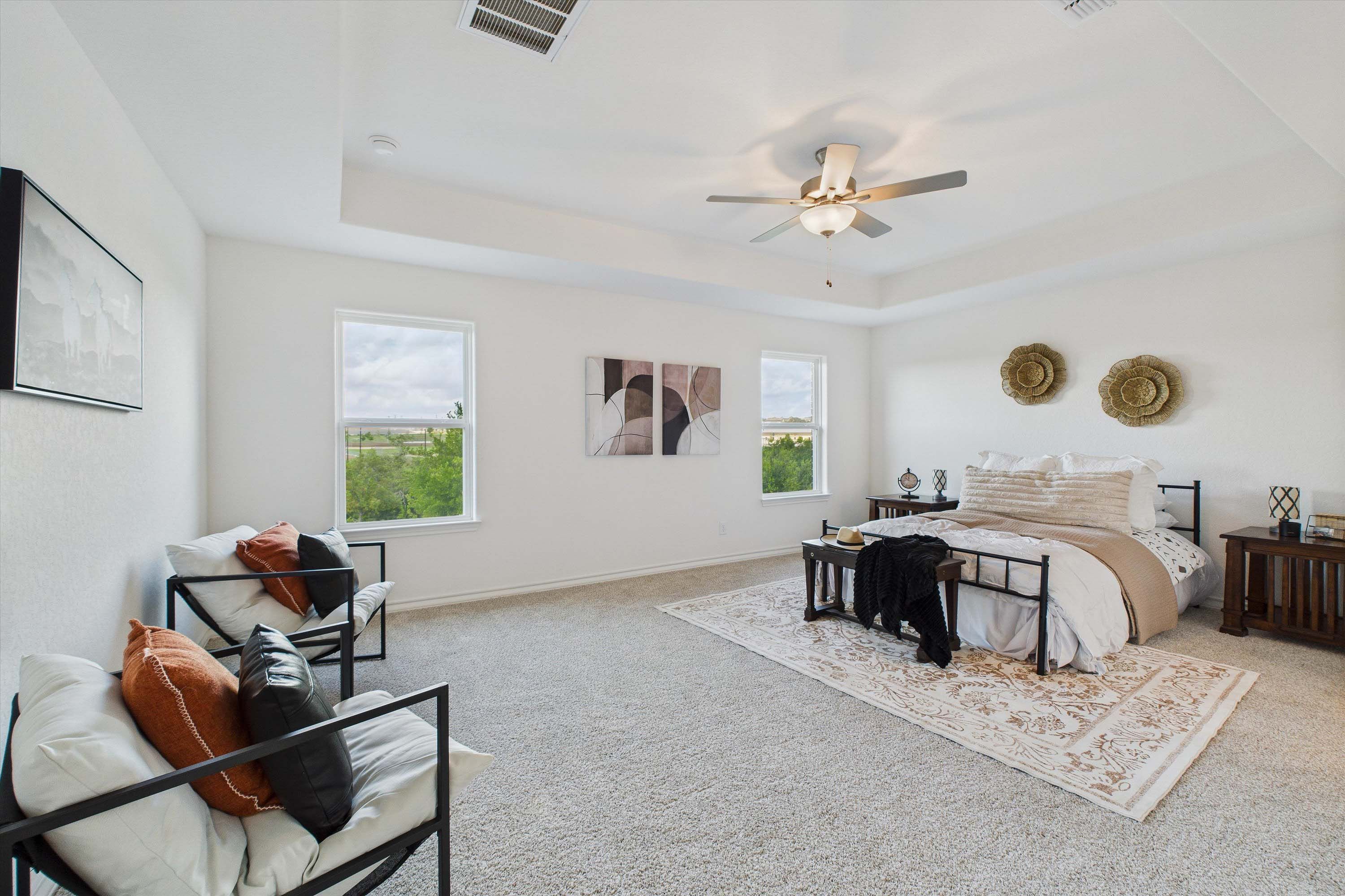 Spacious master suite in The Danbury home design featuring a tray ceiling, plush carpet, and a cozy sitting area.