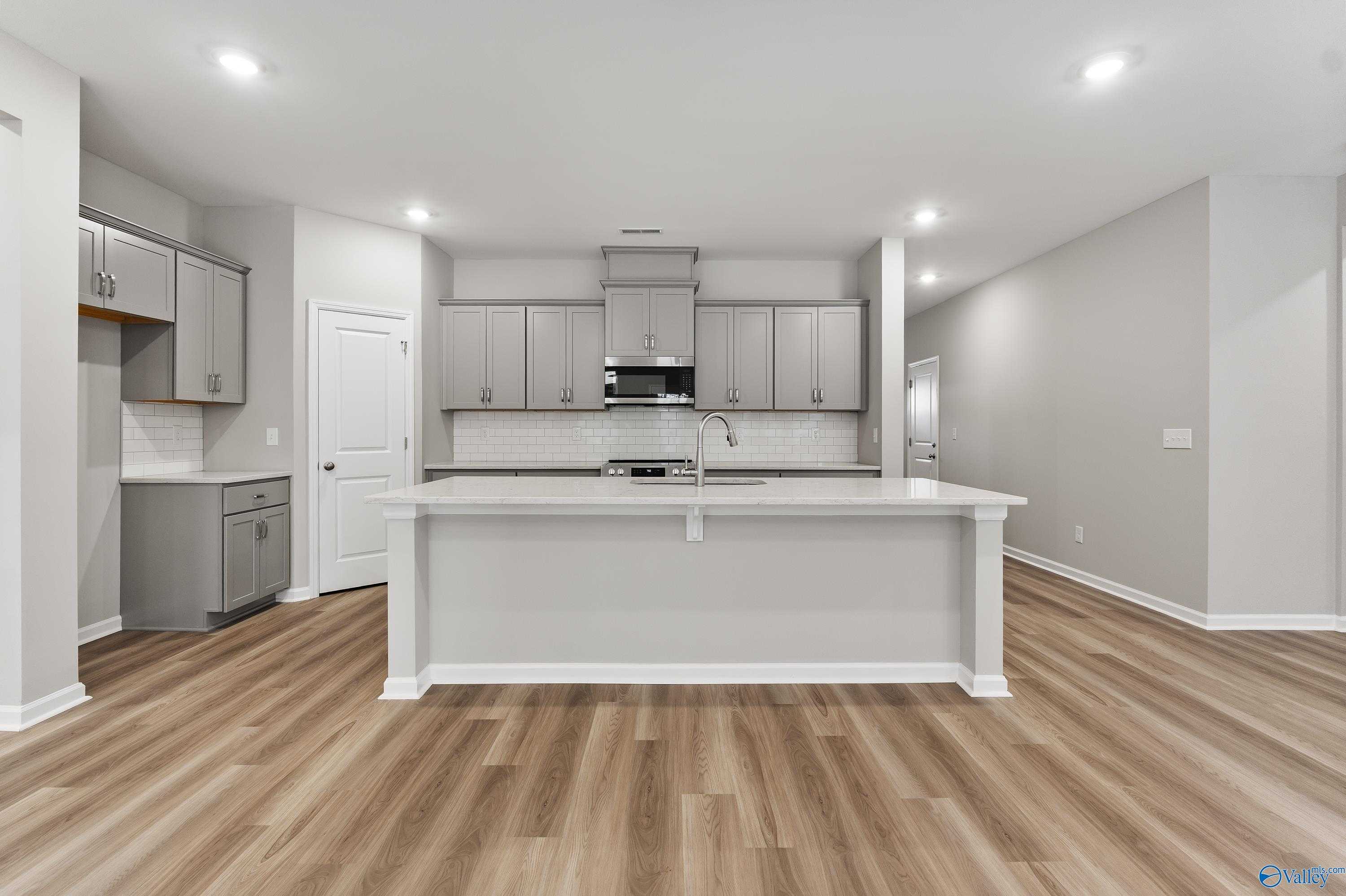 Modern open-concept kitchen featuring white island, stainless appliances, gray cabinets, and wood floors in The Grace plan, Madison, AL