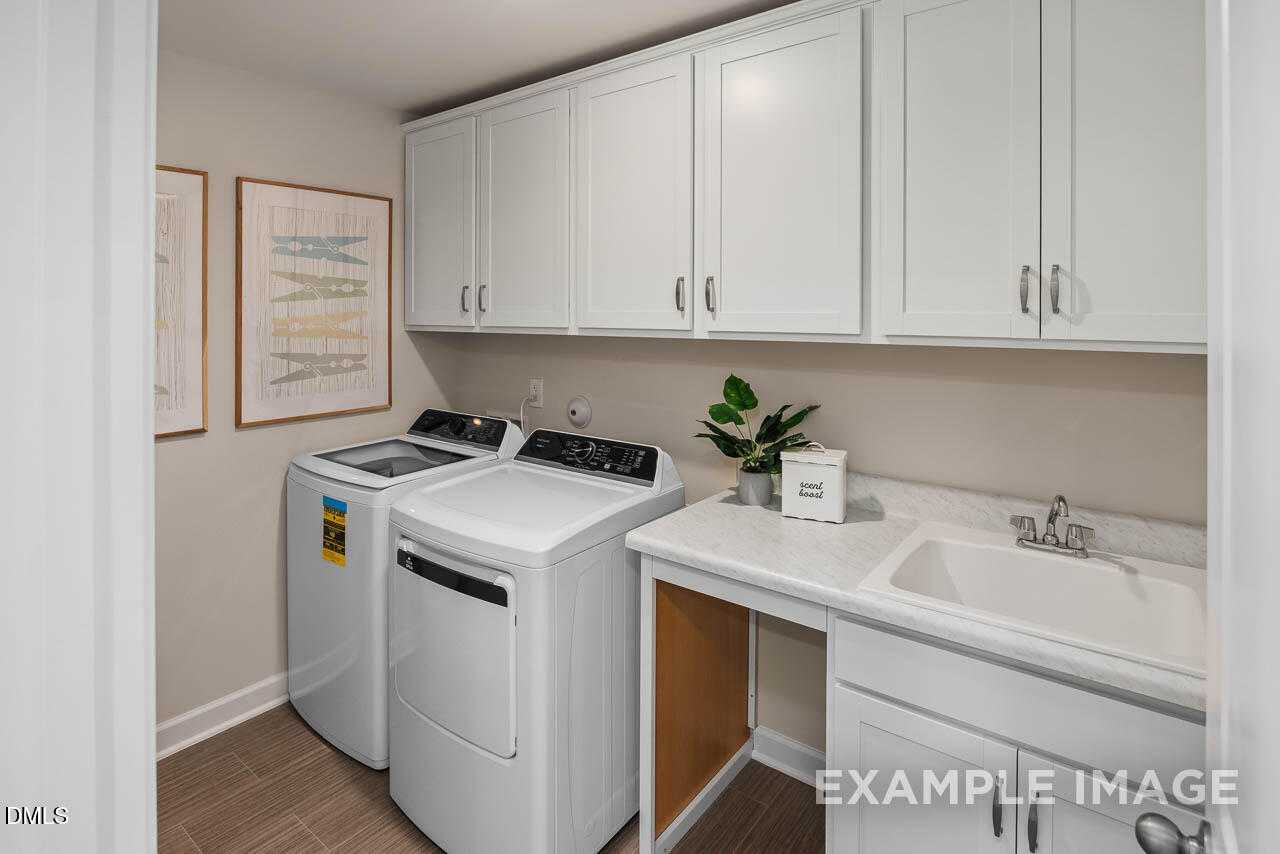 Modern laundry room featuring white washer, dryer, upper cabinets, and utility sink in Davidson Homes The Willow B, Lillington, NC