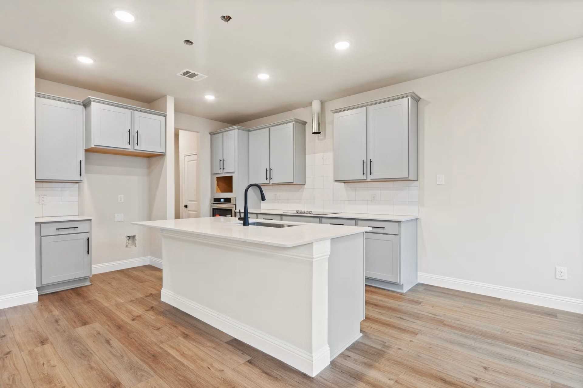 Modern kitchen with gray cabinets, white quartz island, black faucet, and hardwood floors in Davidson Homes The Wake D, Wylie, Texas