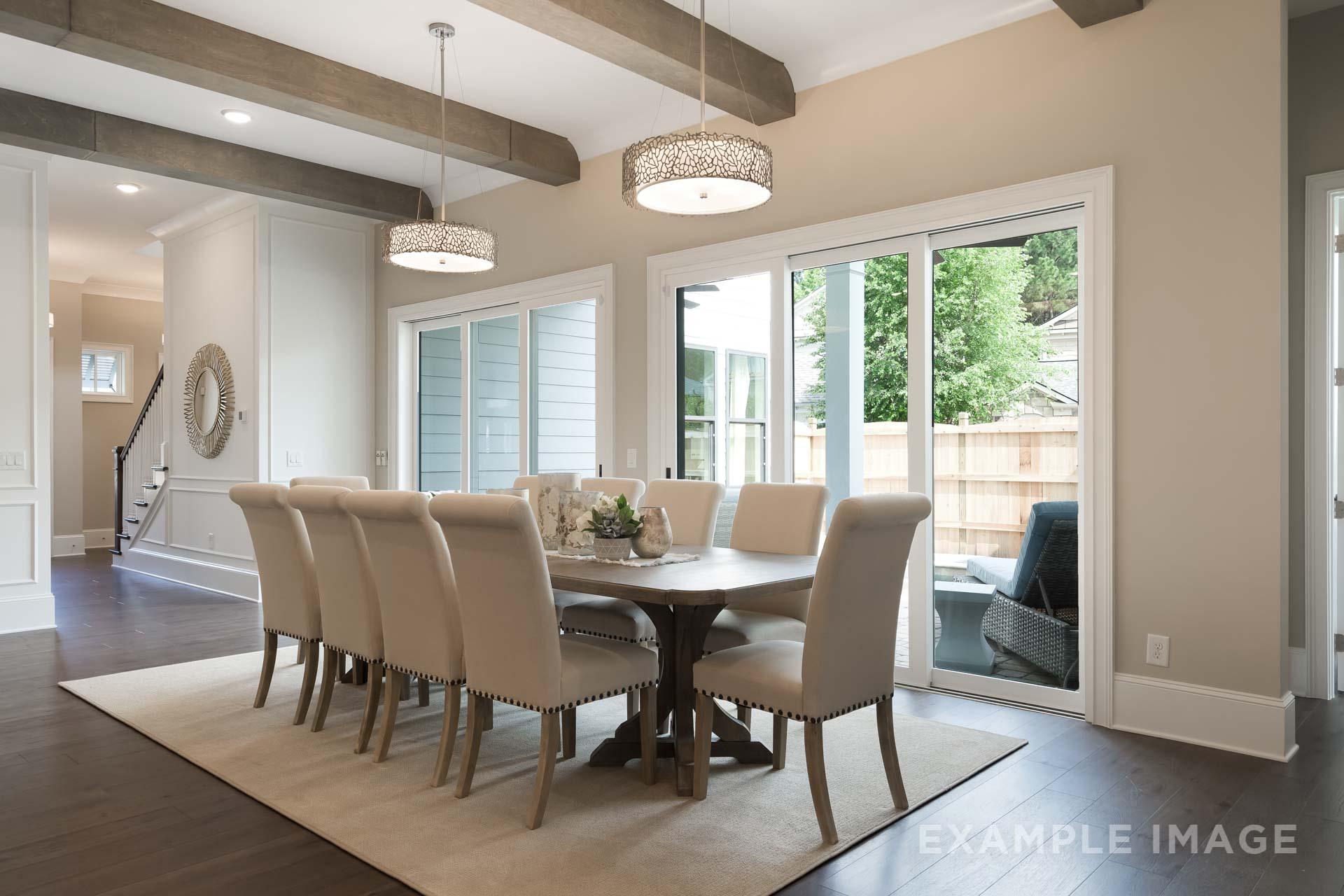 Spacious dining room in The Seaside C featuring farmhouse trestle table, upholstered chairs, exposed beam ceiling, and sliding doors to backyard patio