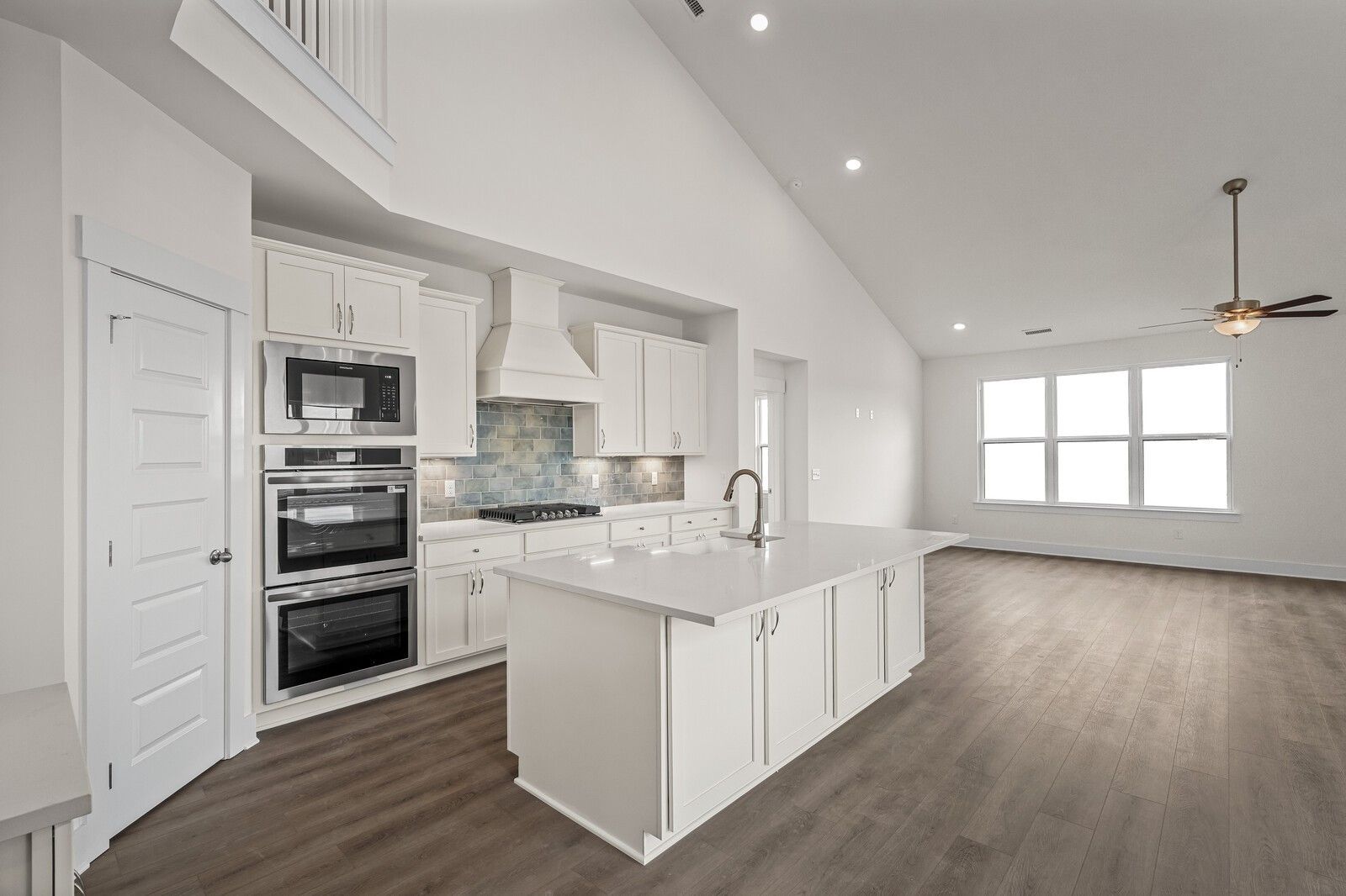 Modern white kitchen featuring quartz island, stainless double oven, subway tile backsplash, and vaulted ceiling in Davidson Homes Ridgeport D, Mt. Juliet, TN