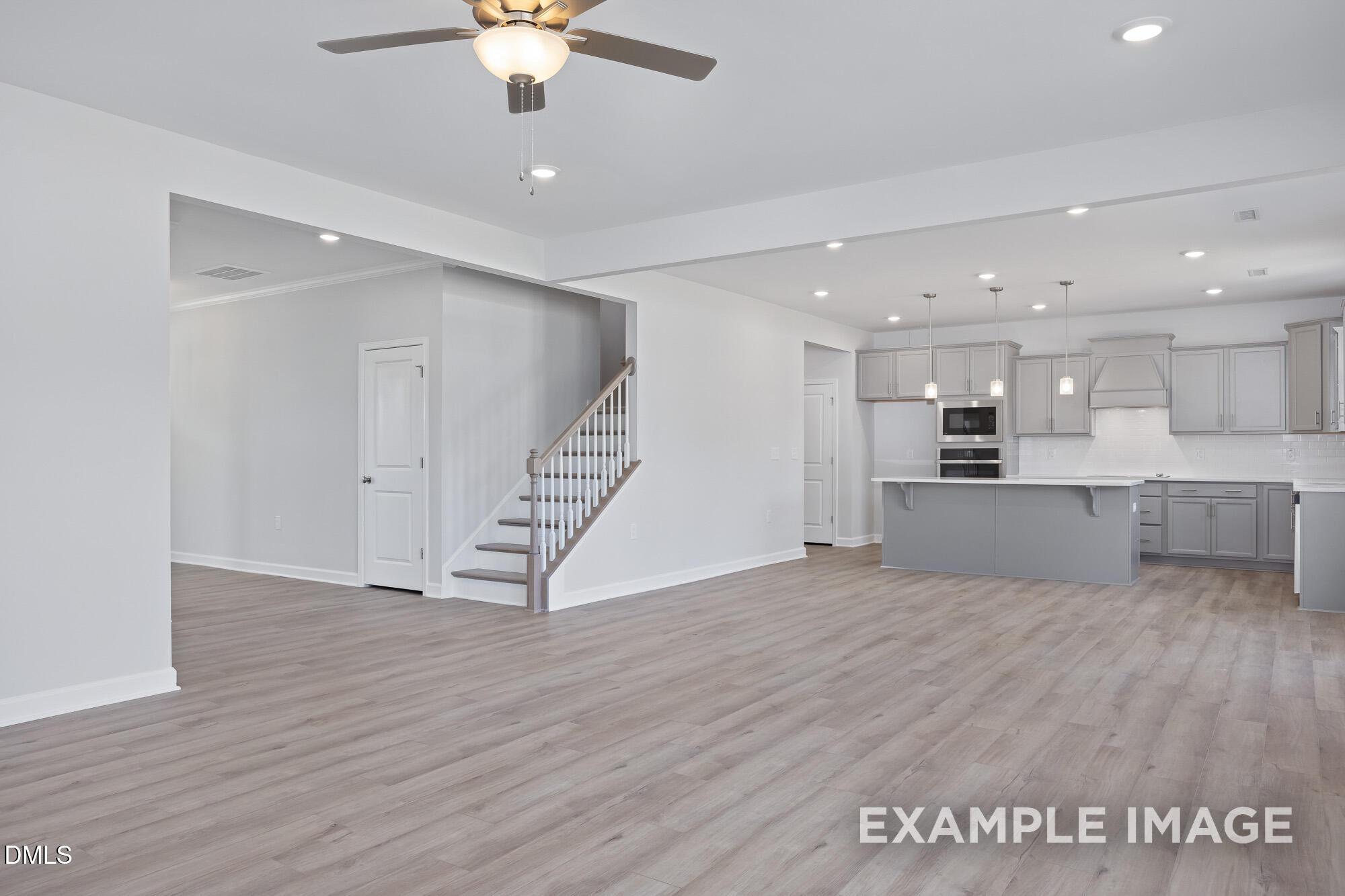 Open-concept living area with modern gray kitchen island, hardwood floors, staircase, and ceiling fan in Davidson Homes The Hickory II B, Lillington, NC