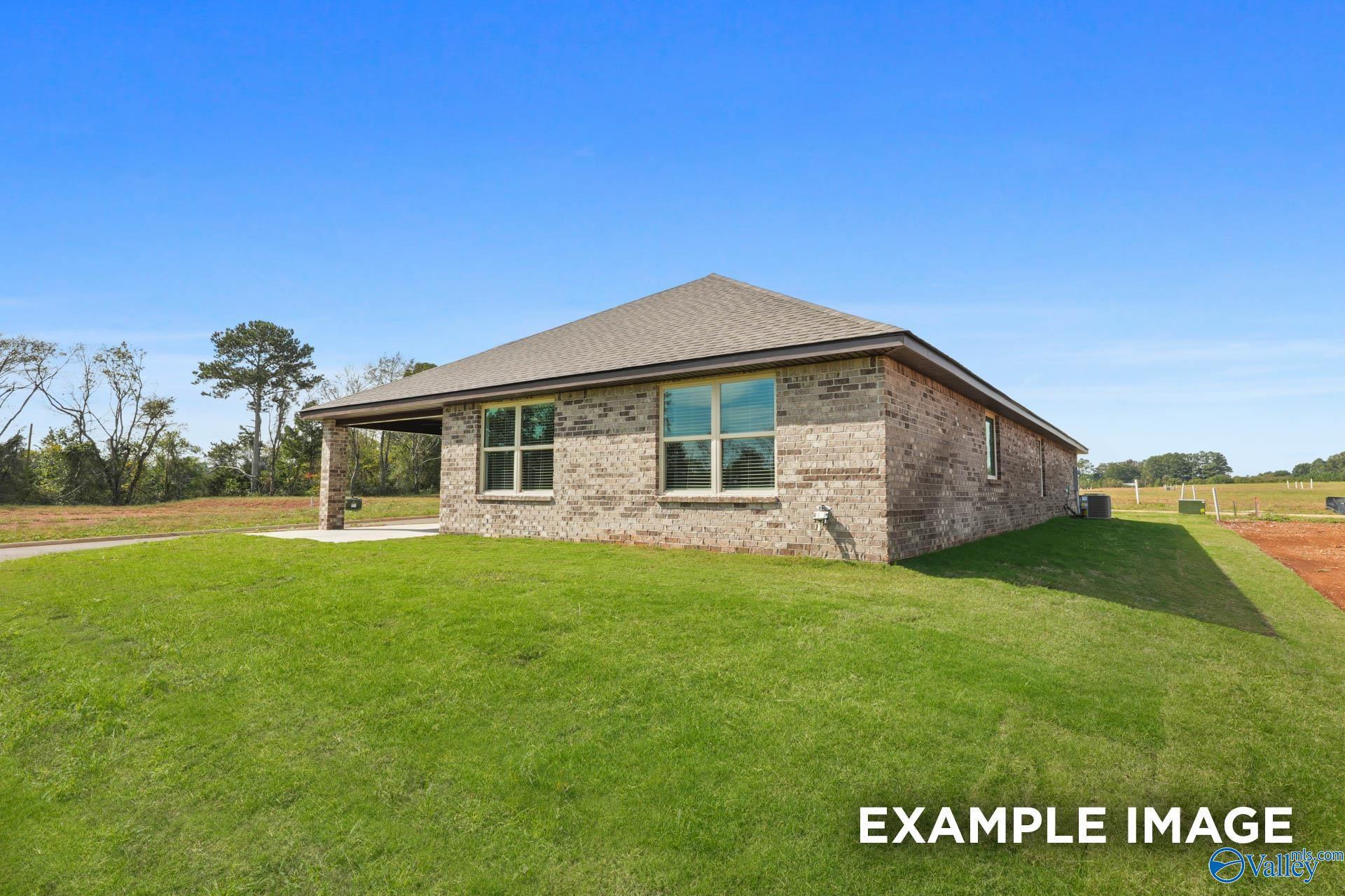 Brick single-story home with gabled roof, large windows, covered garage, and lush green yard in Wood Trail, Toney, Alabama