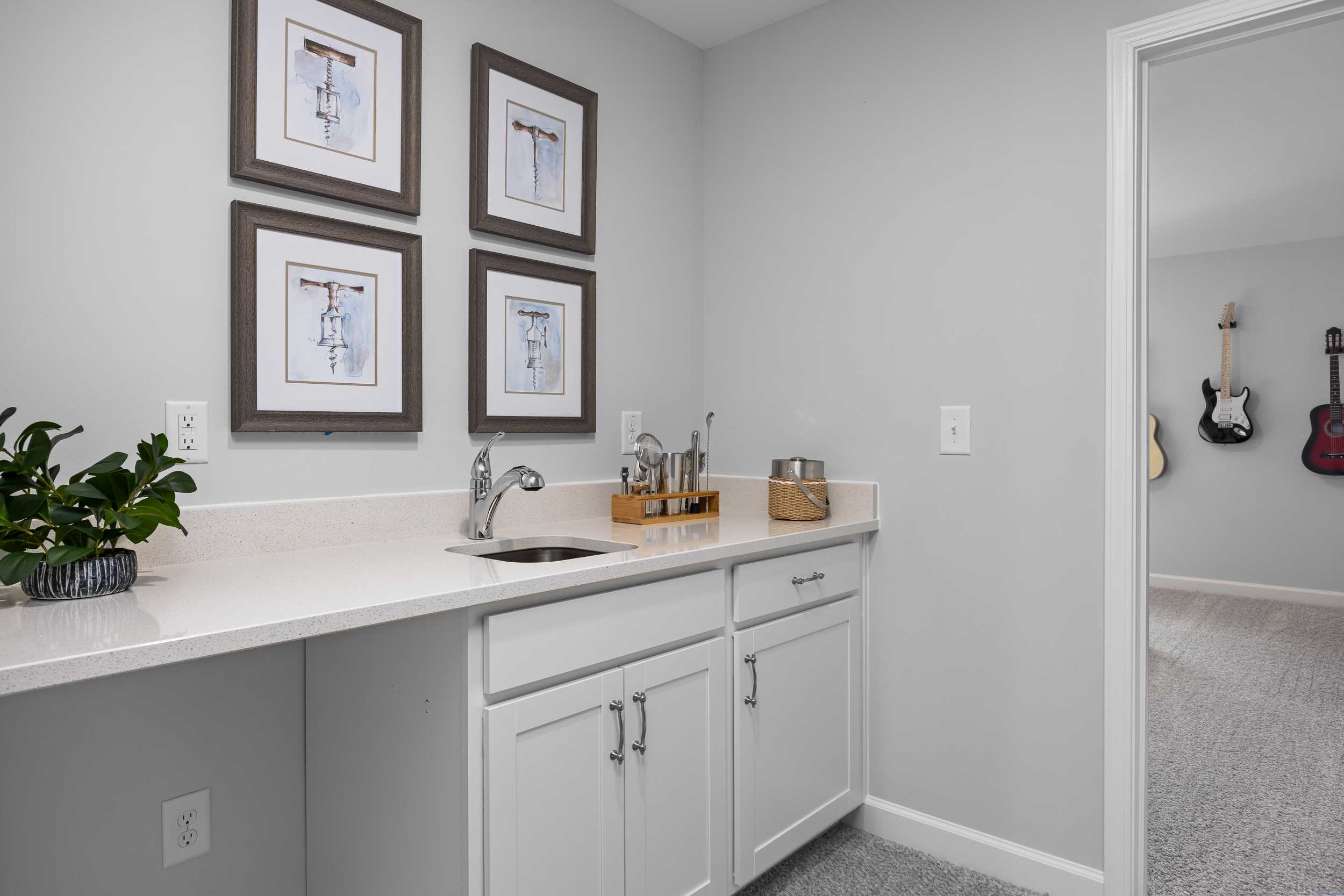 Contemporary wet bar with white cabinets, sink, framed art, and adjacent guitar display in Tobacco Road home, Angier NC