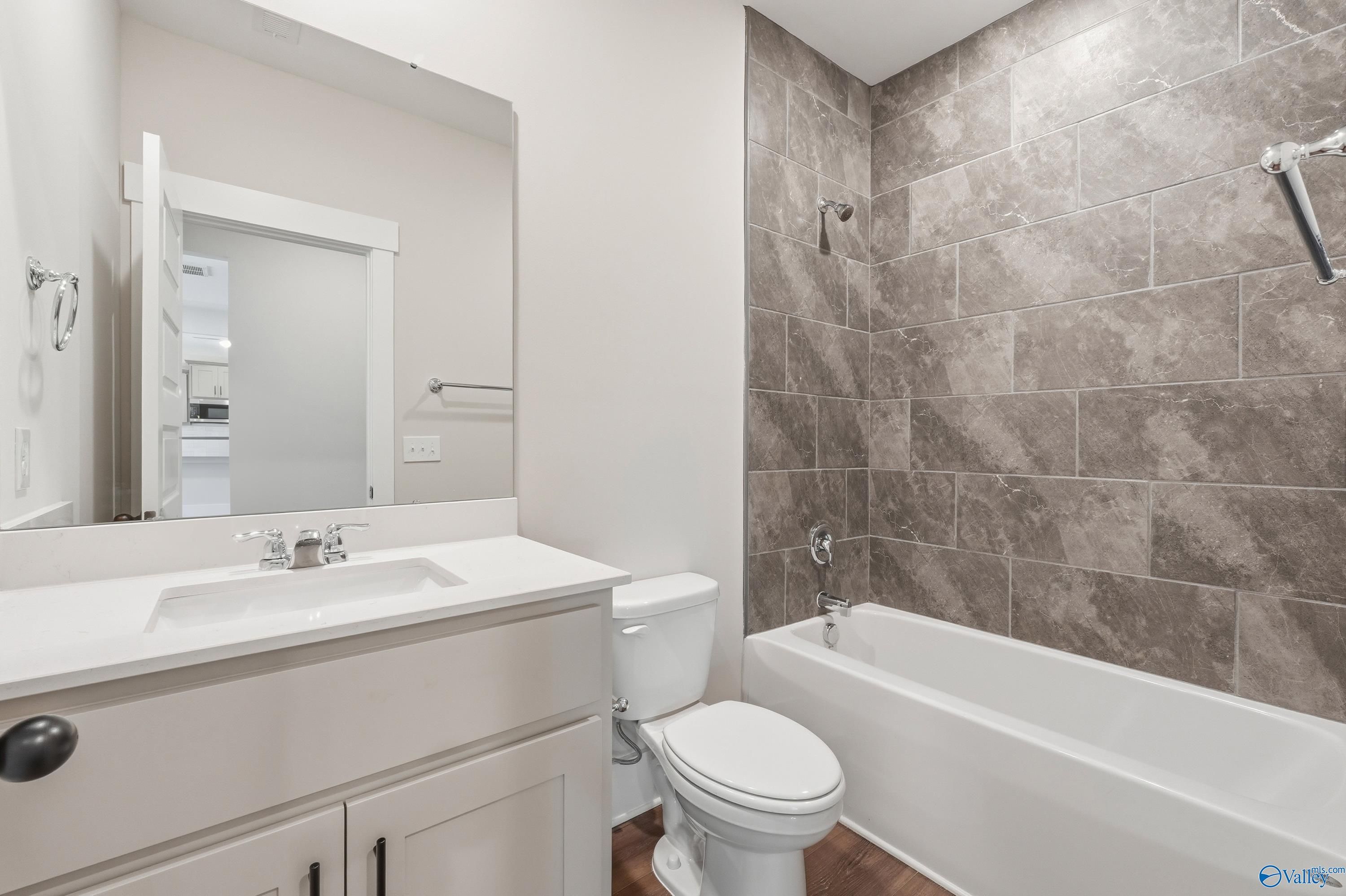 Modern bathroom with deep soaking tub, gray tiled shower, white vanity sink, and toilet in The Shelby A by Davidson Homes, Athens, Alabama