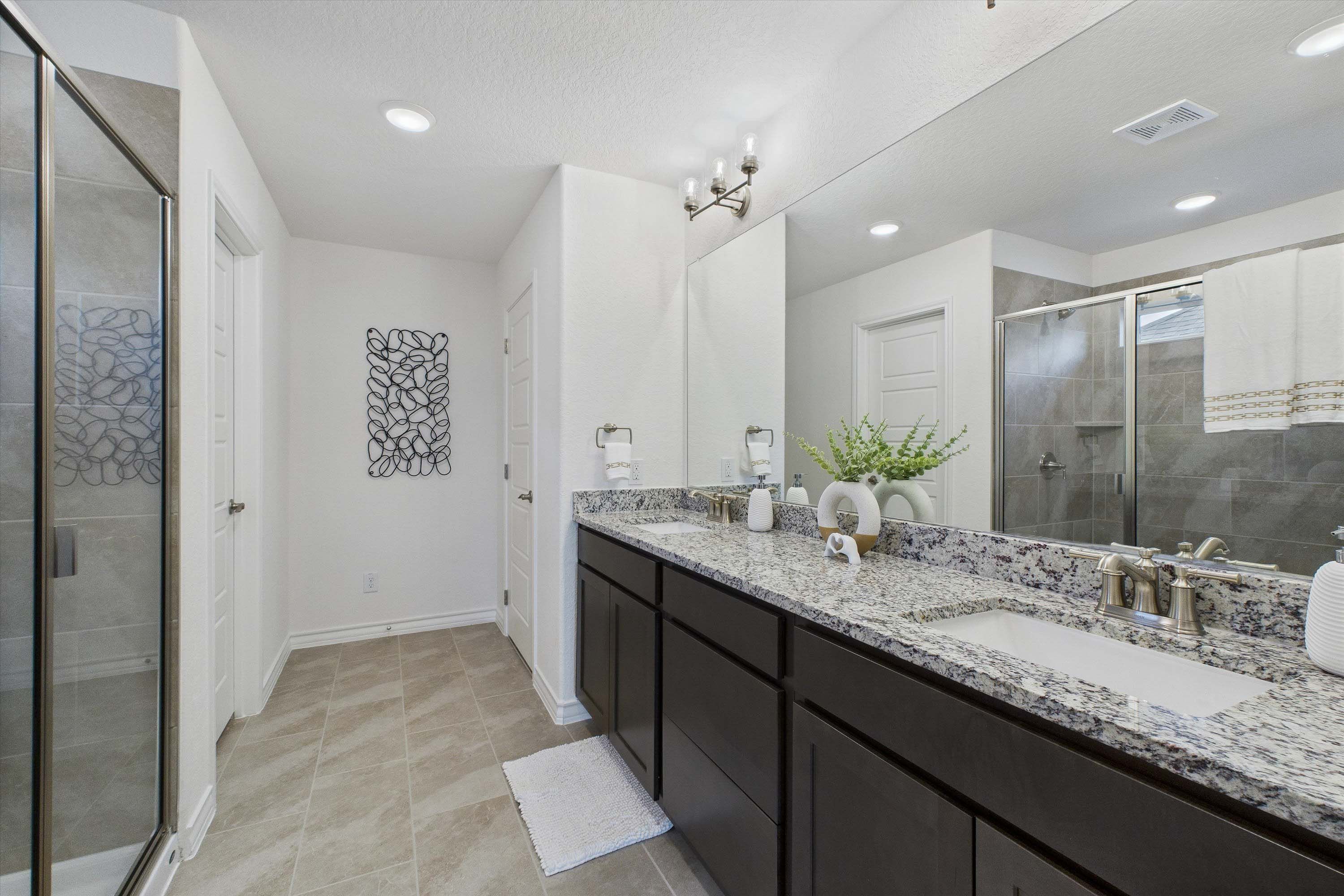 Master bathroom in The Danbury featuring a dual-sink granite vanity, dark cabinetry, and a glass-enclosed walk-in shower.