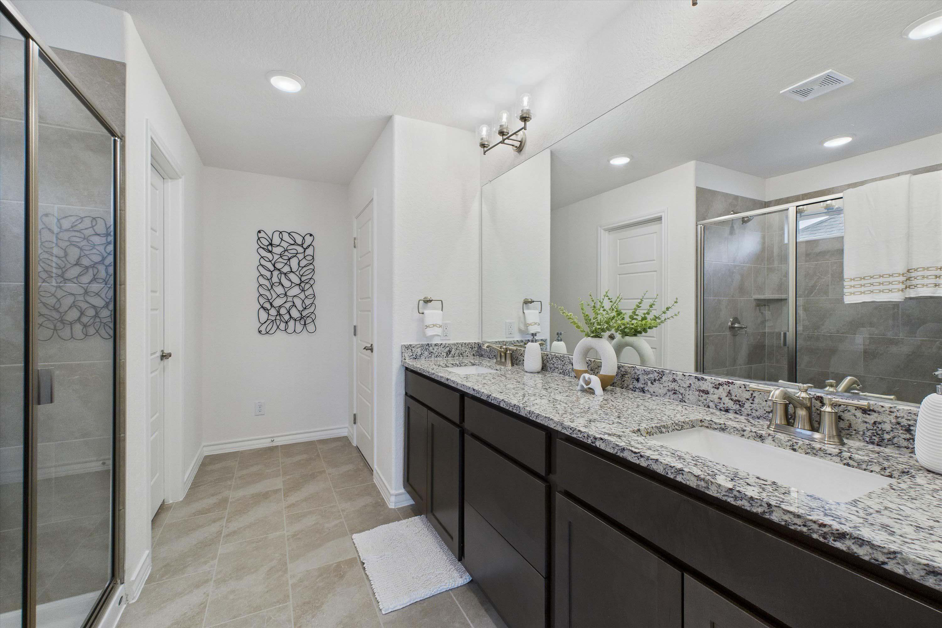 Master bathroom in The Danbury featuring a dual-sink granite vanity, dark cabinetry, and a glass-enclosed walk-in shower.