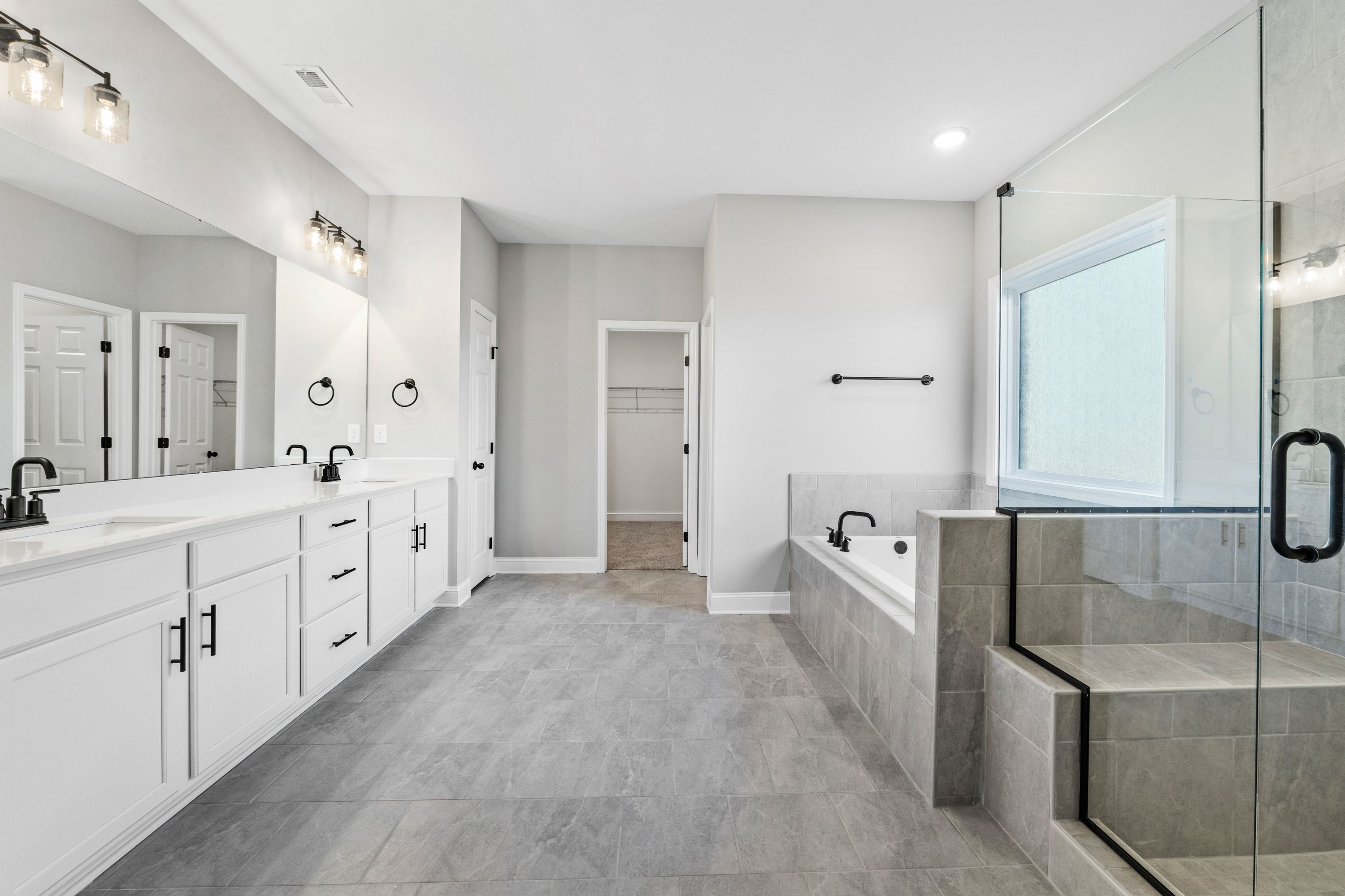 Spacious master bathroom in The Valencia with dual white vanities, soaking tub, glass shower, and neutral gray floors