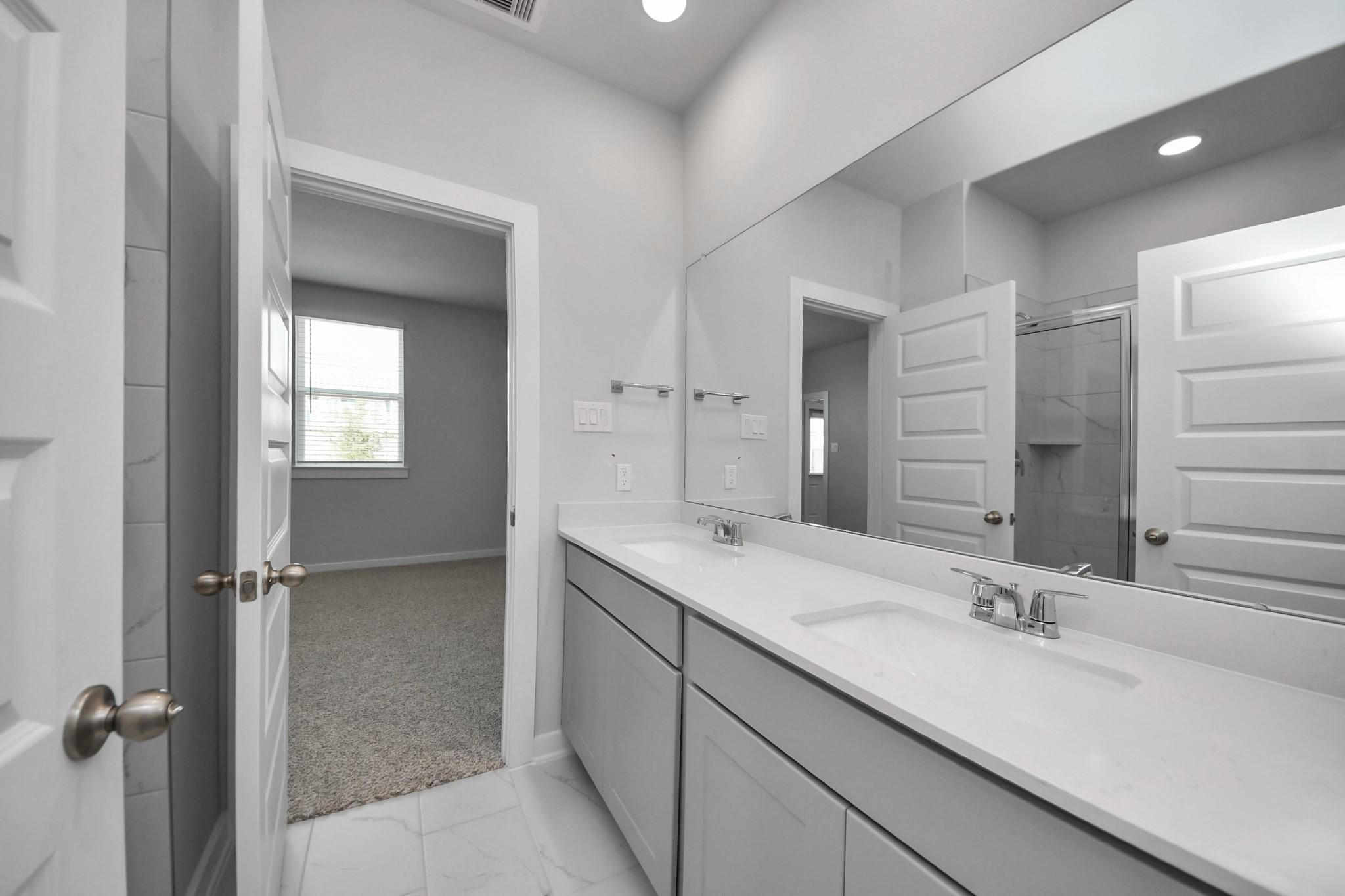 Double vanity bathroom with white quartz countertops and walk-in shower in Davidson Homes The Frio F, Houston, Texas