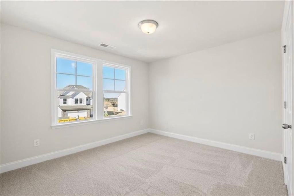 Bright, spacious secondary bedroom with neutral carpet in The Ash C floor plan at Wehunt Meadows, Hoschton, Georgia.