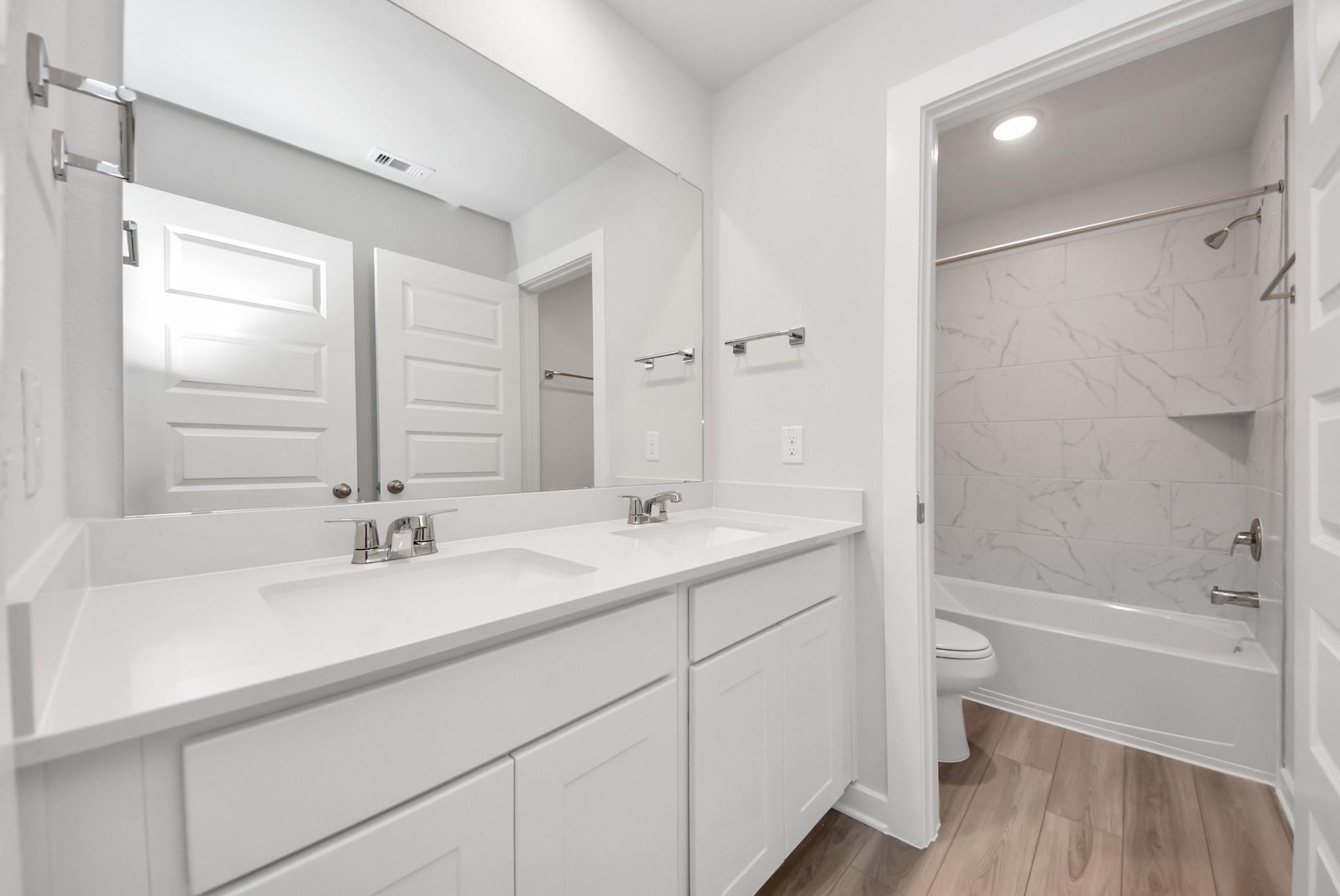 Modern bathroom with dual vanity, white cabinetry, and marble-look tub surround in The Sabine E floor plan, Magnolia, Texas.