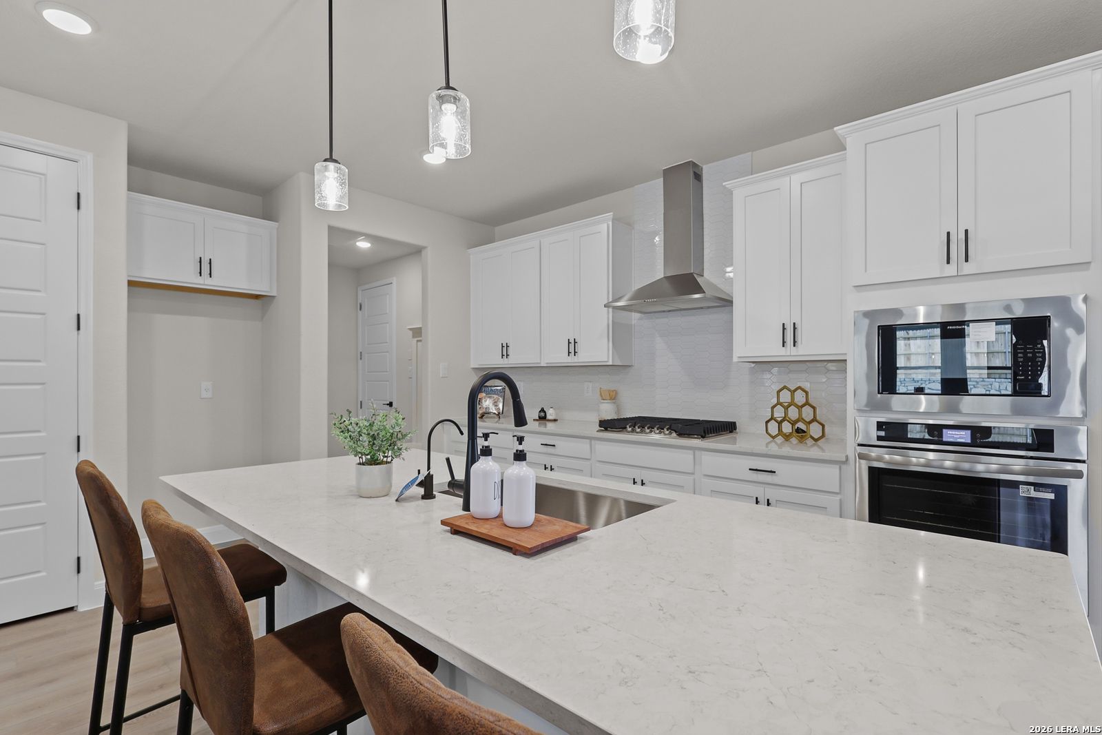 Modern white kitchen with quartz island, stainless appliances, pendant lights in The Lanier G, Castroville, TX