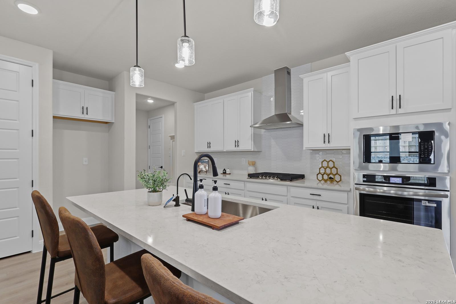 Modern white kitchen with quartz island, stainless appliances, pendant lights in The Lanier G, Castroville, TX