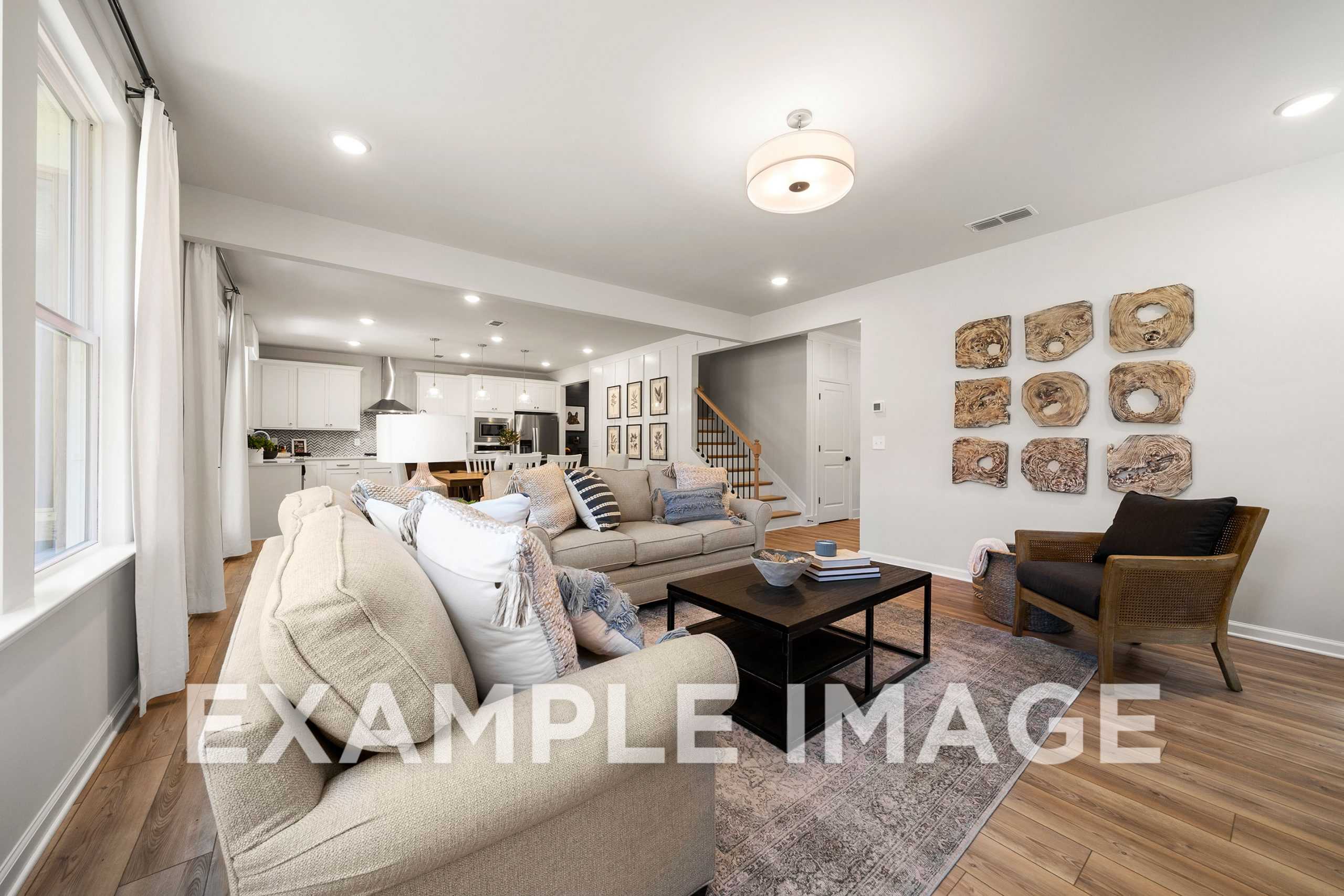 Spacious living room in The Hickory A with plush beige sectional sofa, wooden wall art, coffee table, and open kitchen