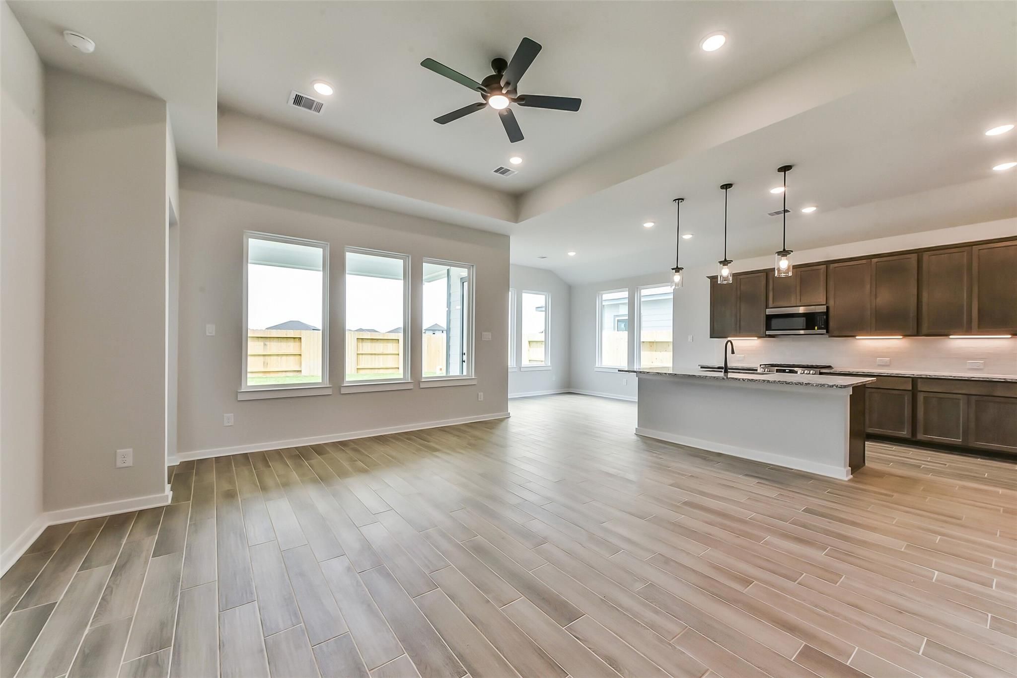 Open-concept kitchen and living area with dark wood cabinets, white island, ceiling fan, and backyard views in Davidson Homes The Sequoia C, Crosby, Texas