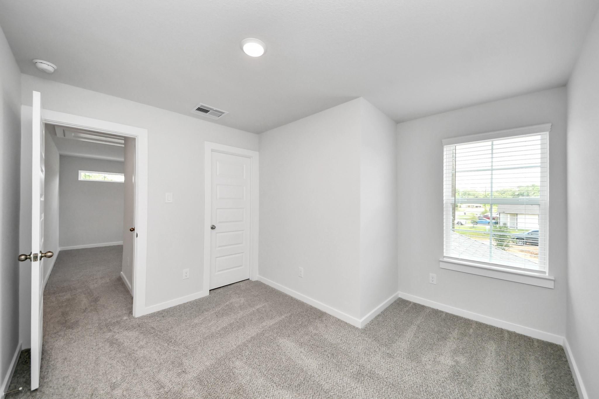 Bright, carpeted bedroom with white walls and natural light in The Sabine E floor plan at Liberty Estates, Cleveland, TX.
