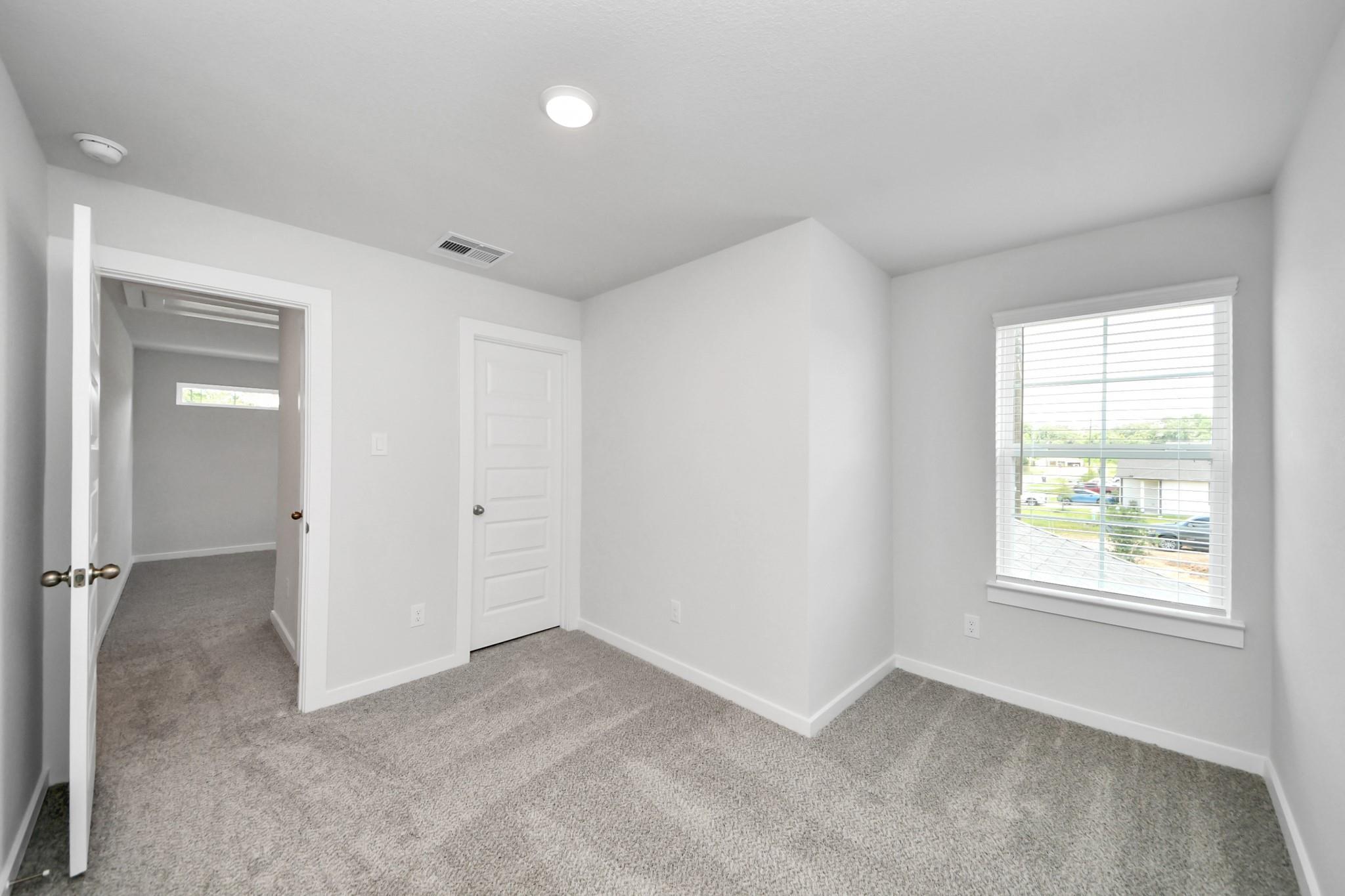 Bright, carpeted bedroom with white walls and natural light in The Sabine E floor plan at Liberty Estates, Cleveland, TX.