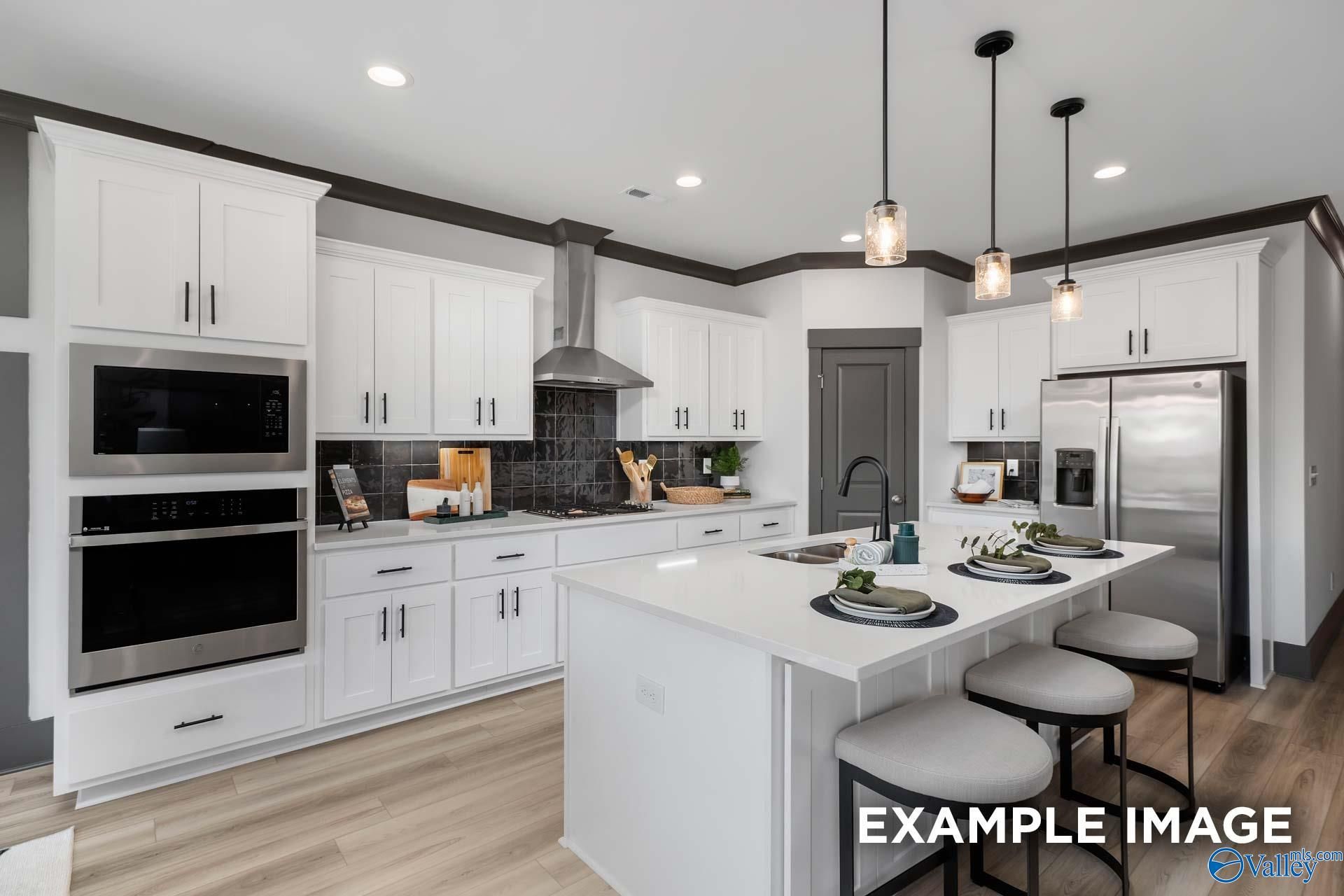 Modern kitchen with white cabinets, stainless steel appliances, large island and pendant lights in Davidson Homes The Rockford B, Madison AL