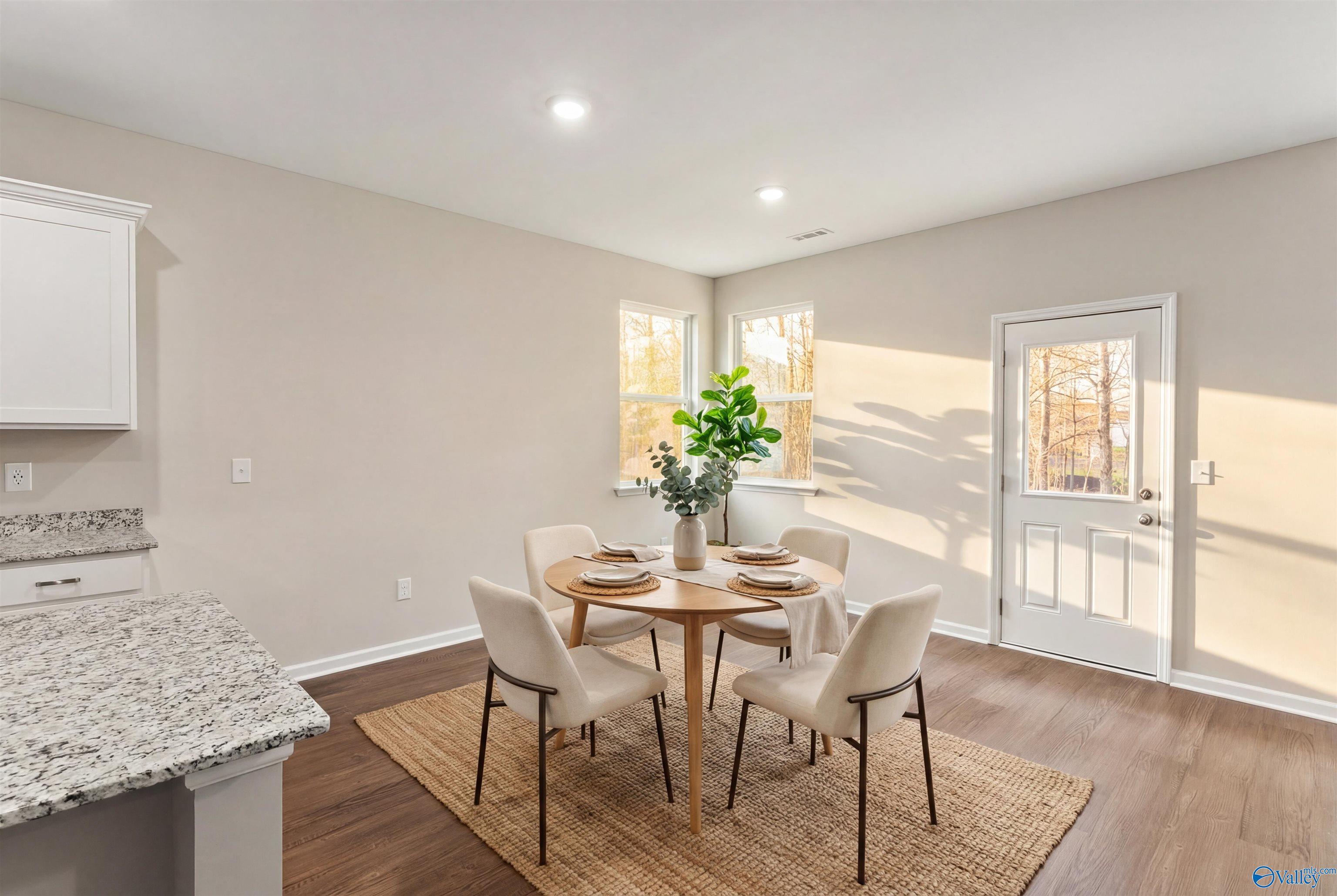 Elegant dining room with round wooden table, white chairs, and floral centerpiece beside granite kitchen in The Phoenix 3-bedroom home, Fayetteville, TN