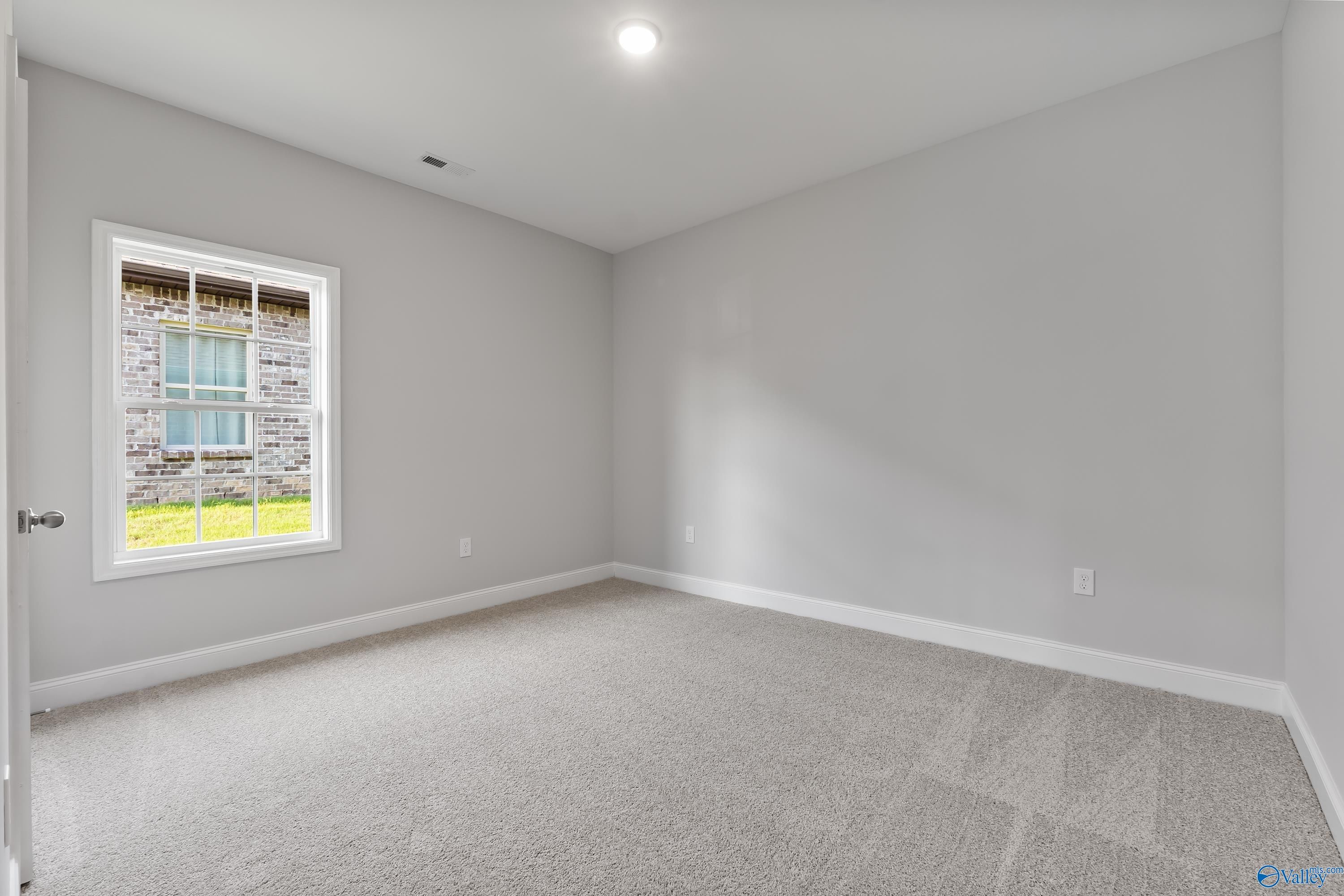 Spacious empty bedroom with light gray walls, beige carpet, large window overlooking green lawn in Davidson Homes The Daphne C, Huntsville AL