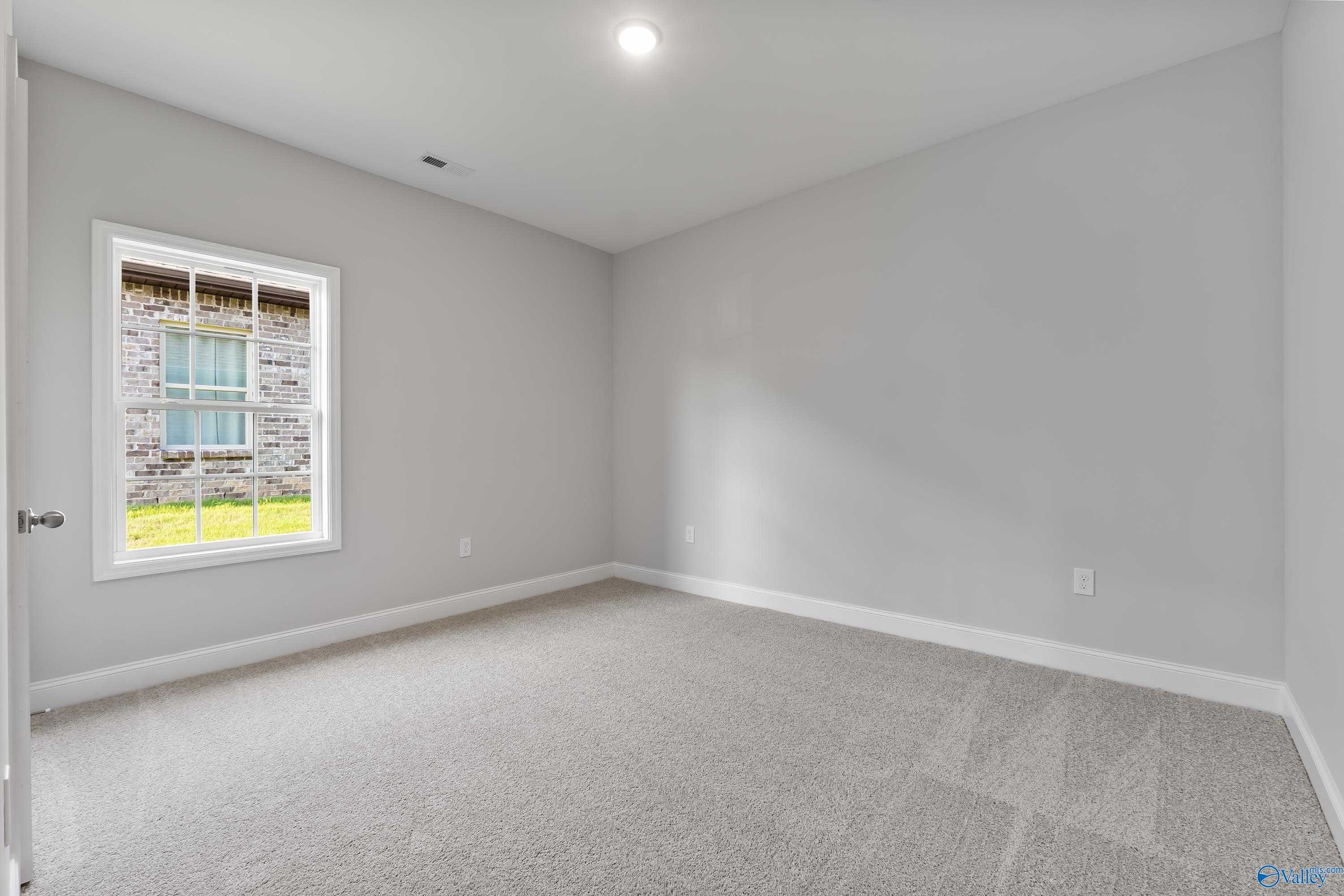 Spacious empty bedroom with light gray walls, beige carpet, large window overlooking green lawn in Davidson Homes The Daphne C, Huntsville AL