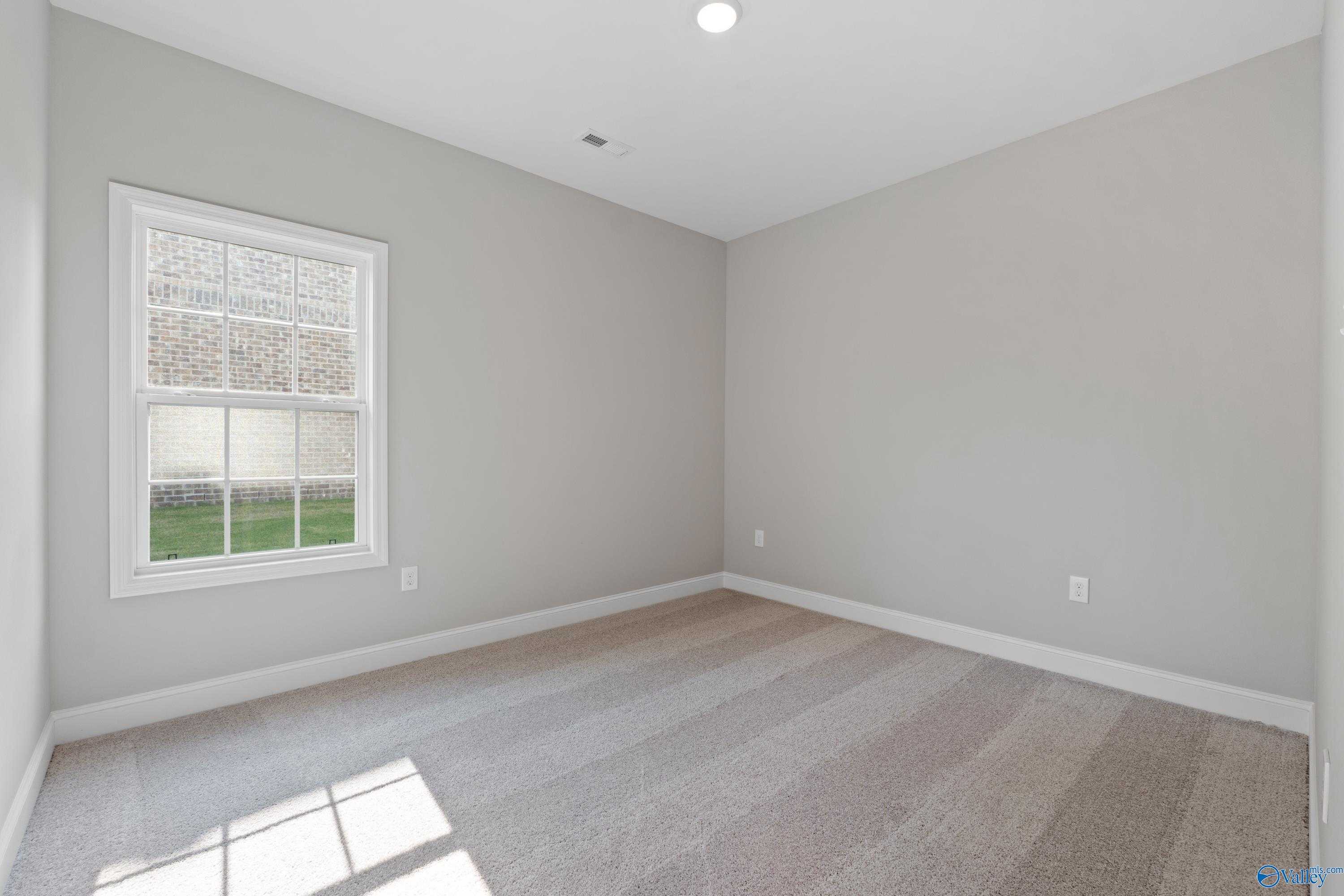 Bright empty bedroom featuring gray walls, large window with yard view, and beige carpet in Davidson Homes The Rockford, Toney, Alabama