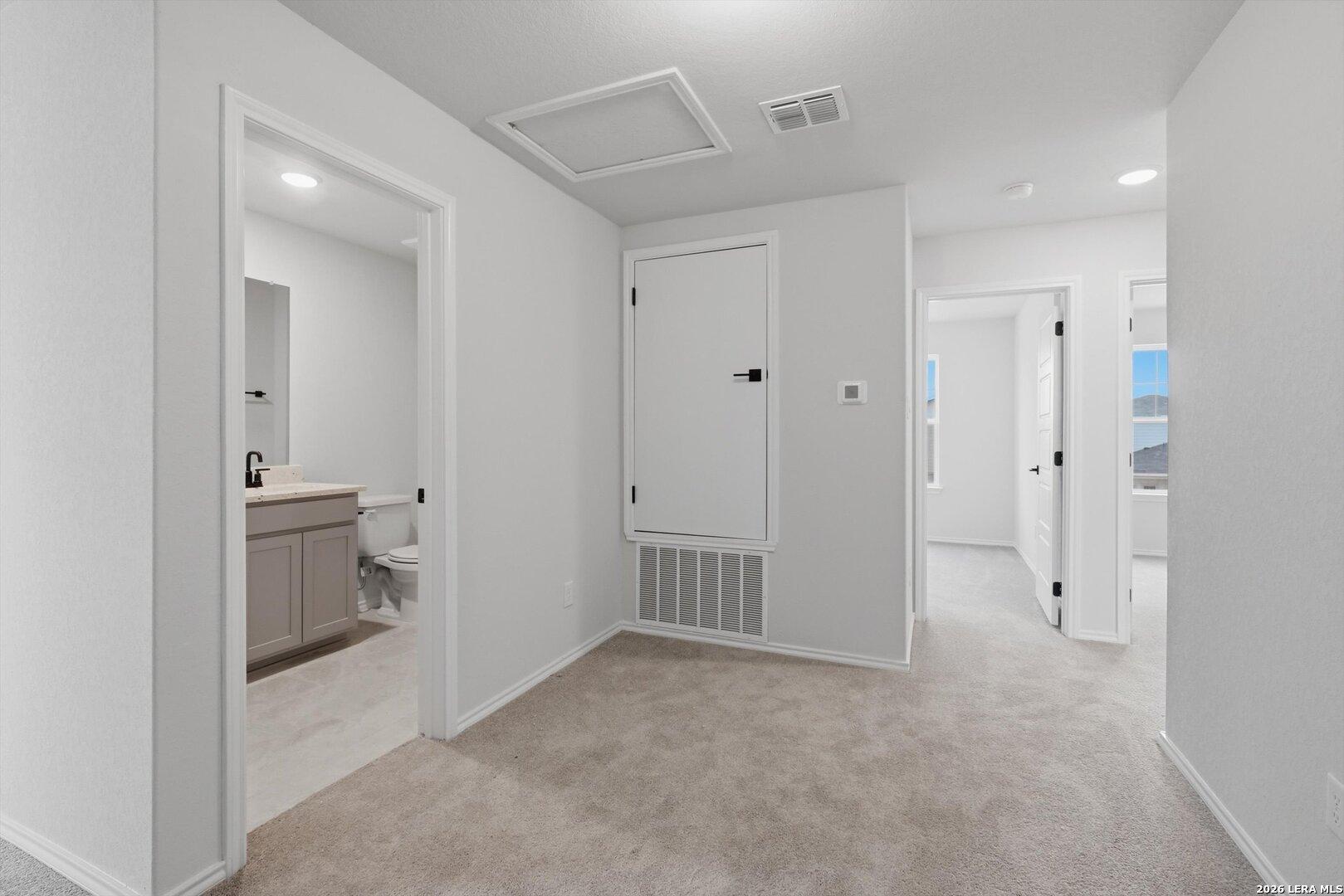 Upstairs carpeted hallway with doors to bedrooms and guest bathroom featuring vanity sink in Davidson Homes The Blanco C, San Antonio