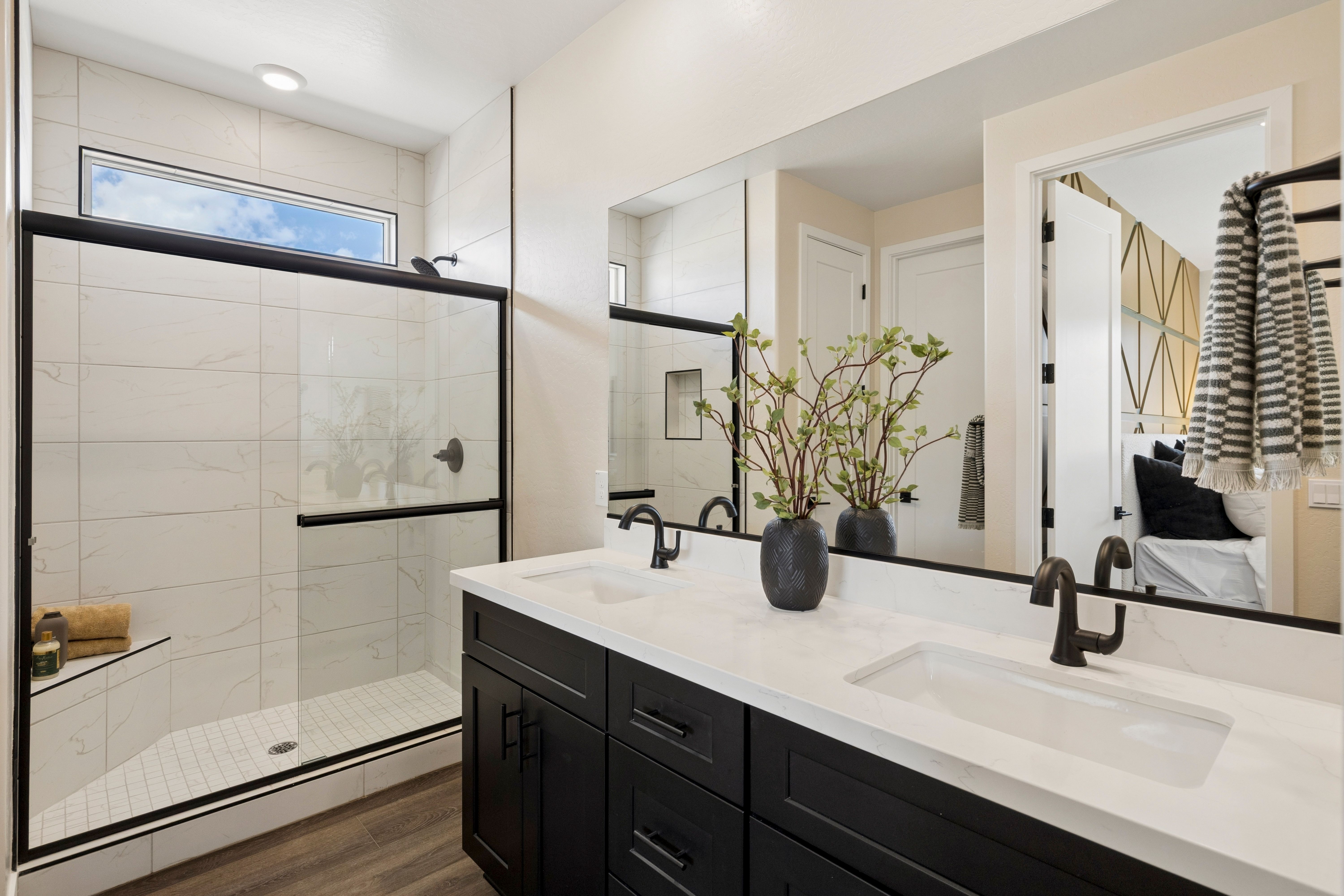 Spacious master bathroom at South Ranch Western Collection in Prescott AZ with frameless glass shower, double black vanity, and potted branch
