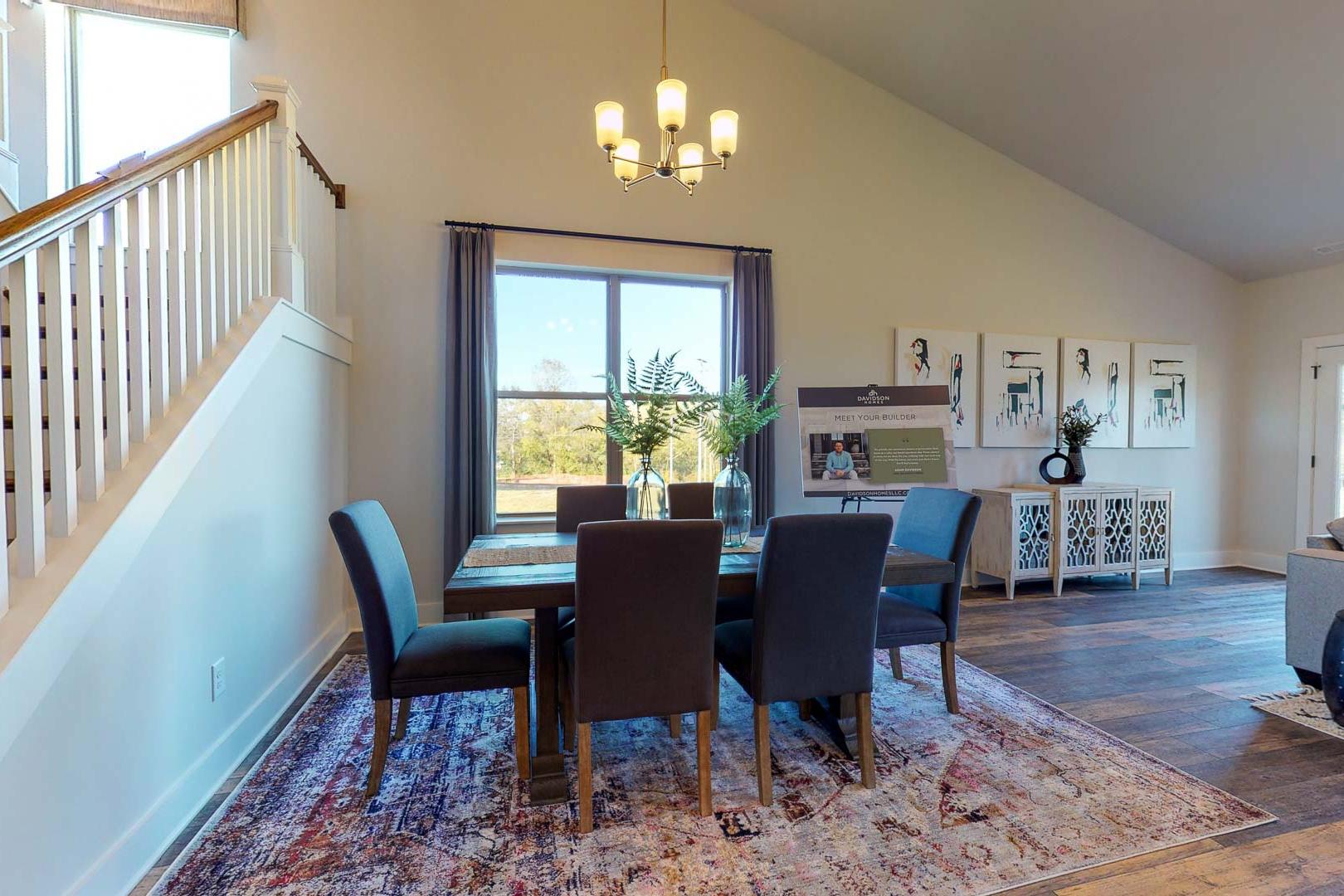 Open dining room in Liberty Creek Gallatin TN home with wooden floors, upholstered chairs, chandelier, large window, and staircase