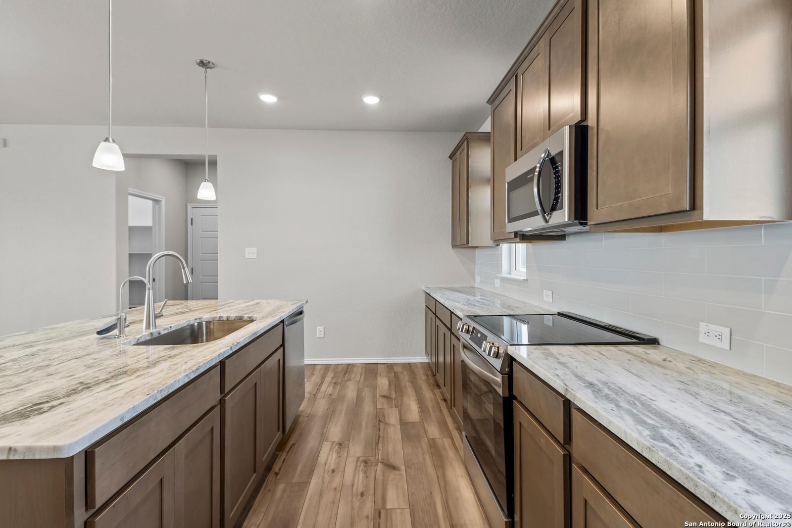 Modern kitchen featuring quartz island sink, stainless steel appliances, shaker cabinets, and hardwood floors in The Collin B, Seguin, TX