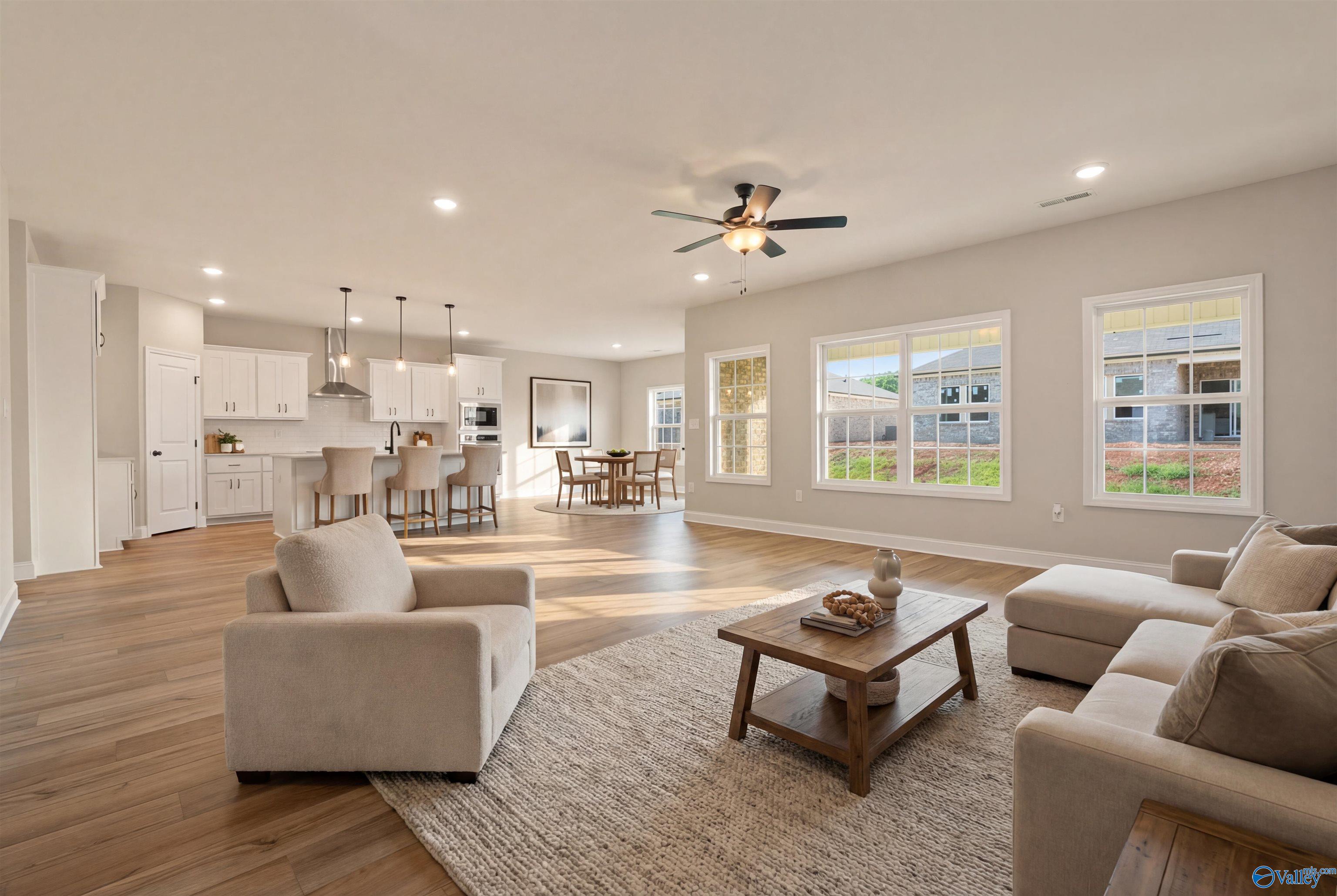 Open-concept living and dining area with white kitchen island, beige sectional sofa, hardwood floors in Davidson Homes The Rockford, Toney, Alabama