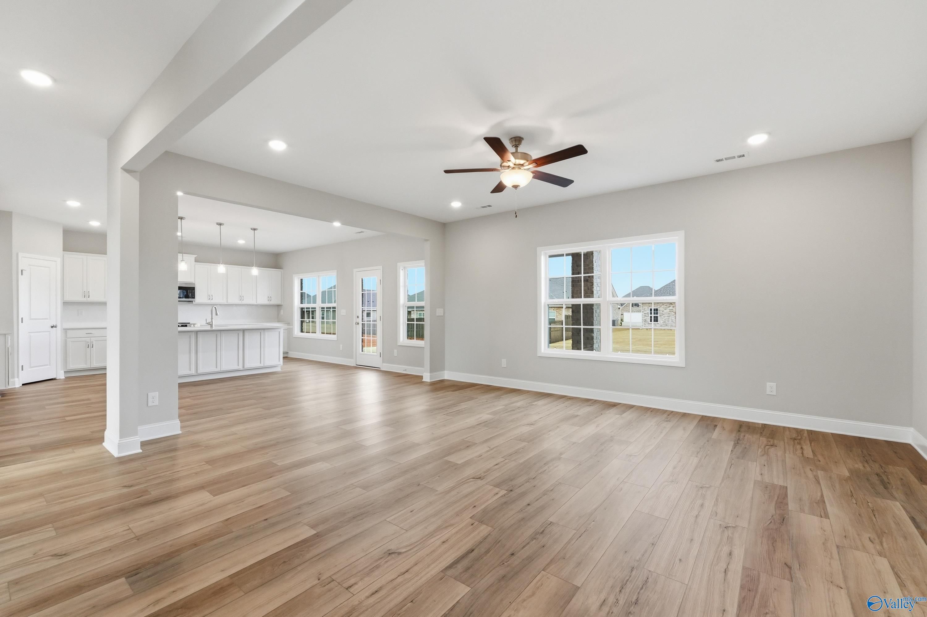 Open-concept living kitchen with white cabinets, hardwood floors, ceiling fan, and large windows in Davidson Homes Madison A, Meridianville