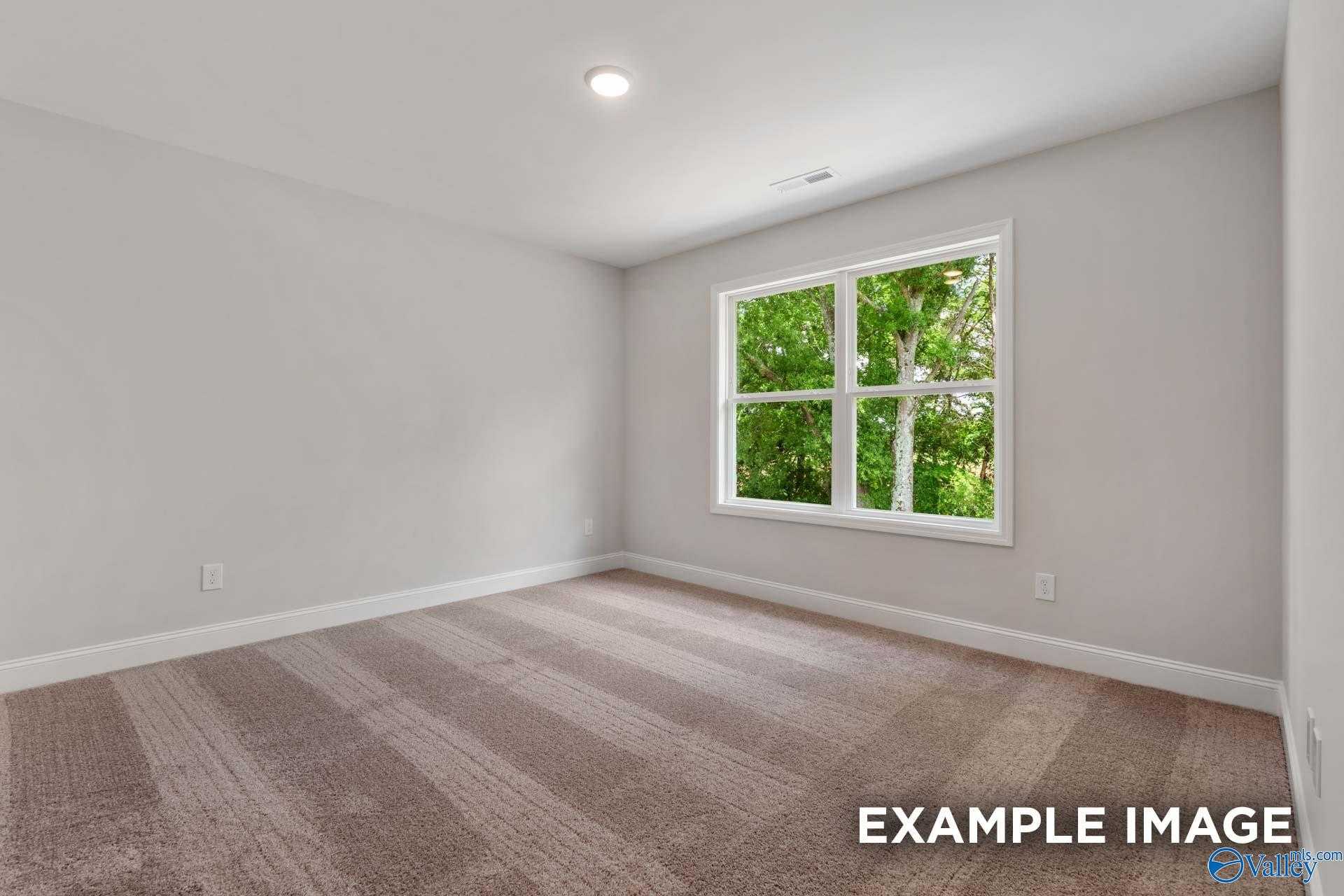 Bright bedroom with neutral walls, plush carpet, and large window overlooking trees in Davidson Homes Shelby C, Meridianville AL