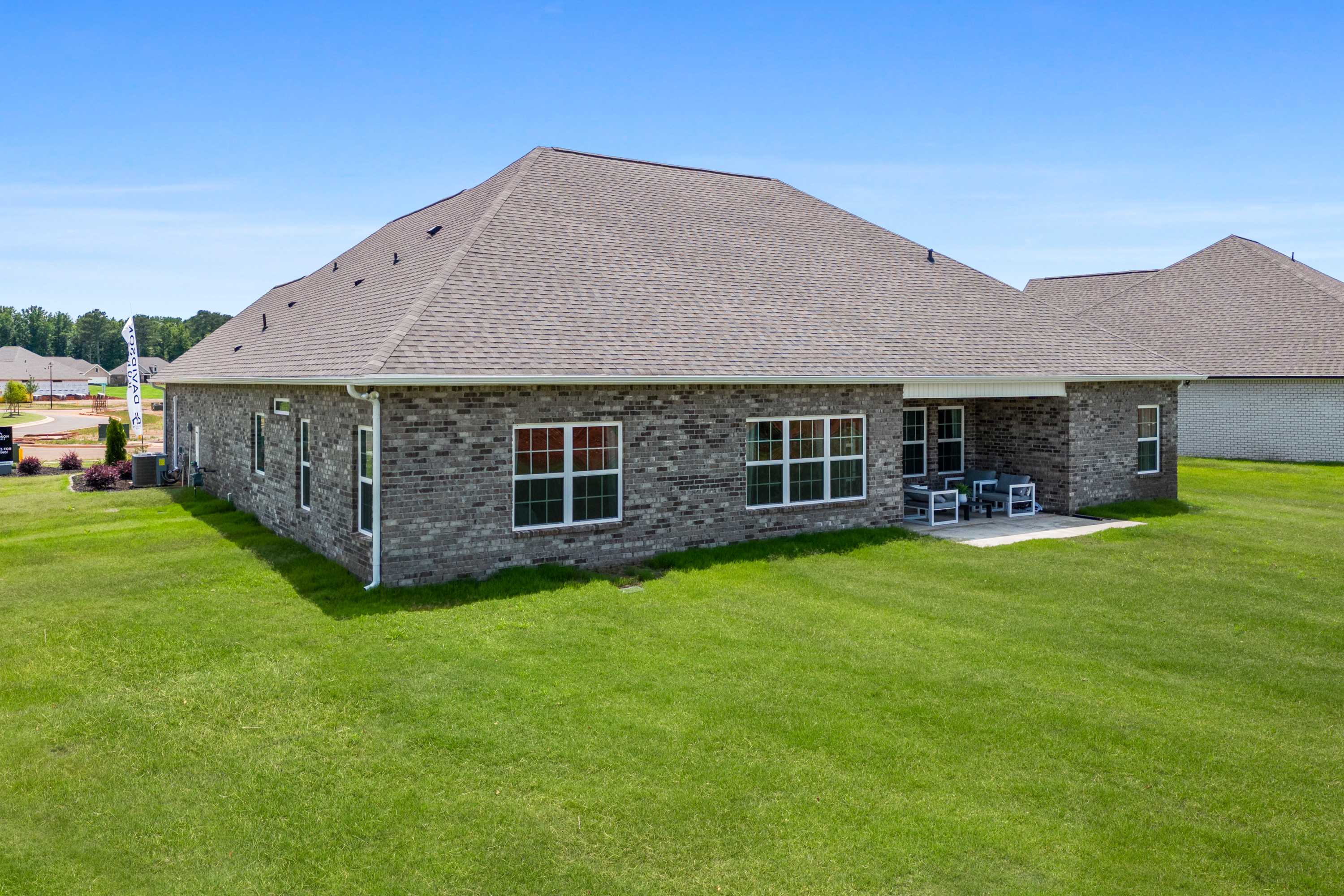 Brick single-story home exterior at Creekside in Harvest Alabama with covered side patio, white chairs, and lush green lawn