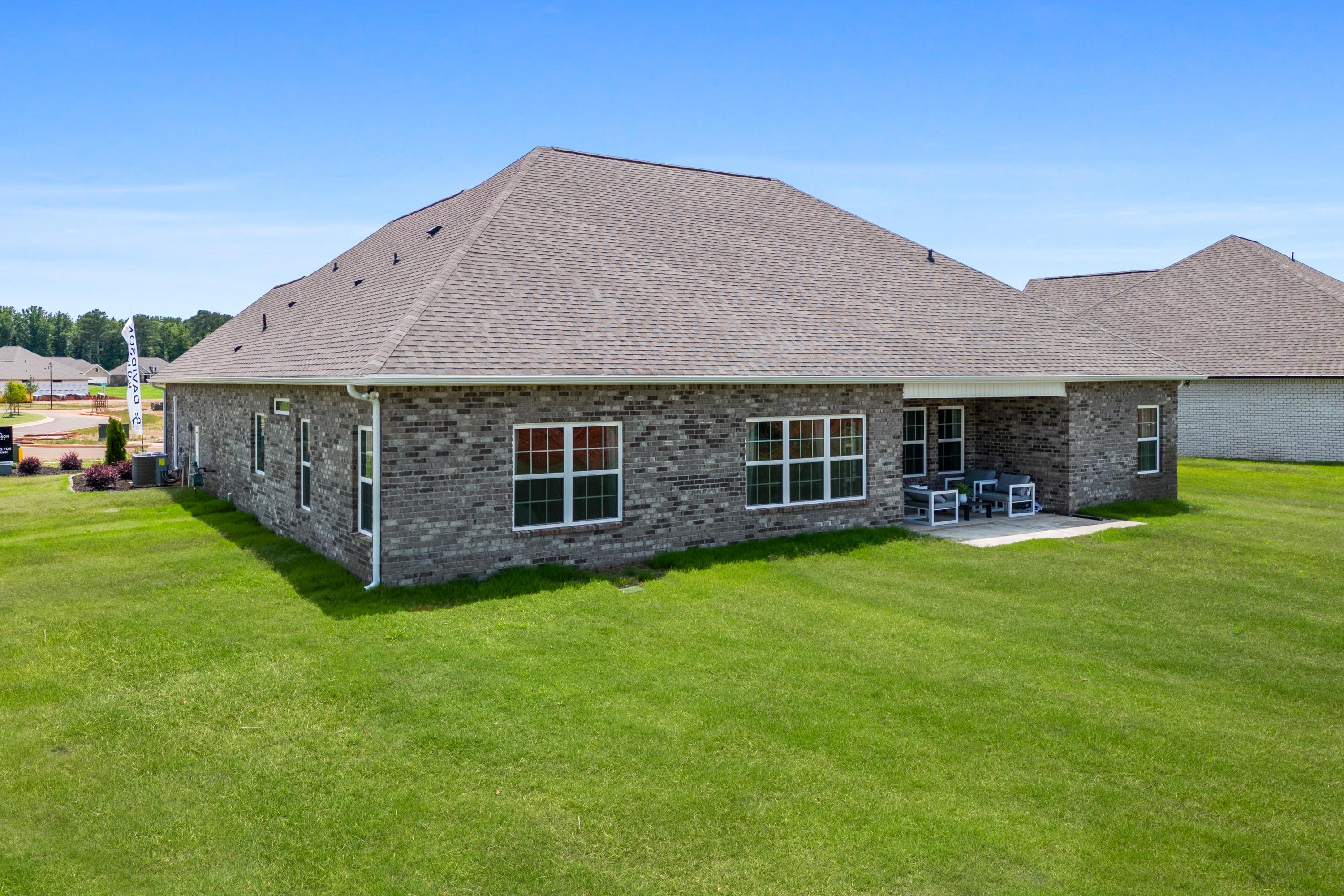 Brick single-story home exterior at Creekside in Harvest Alabama with covered side patio, white chairs, and lush green lawn