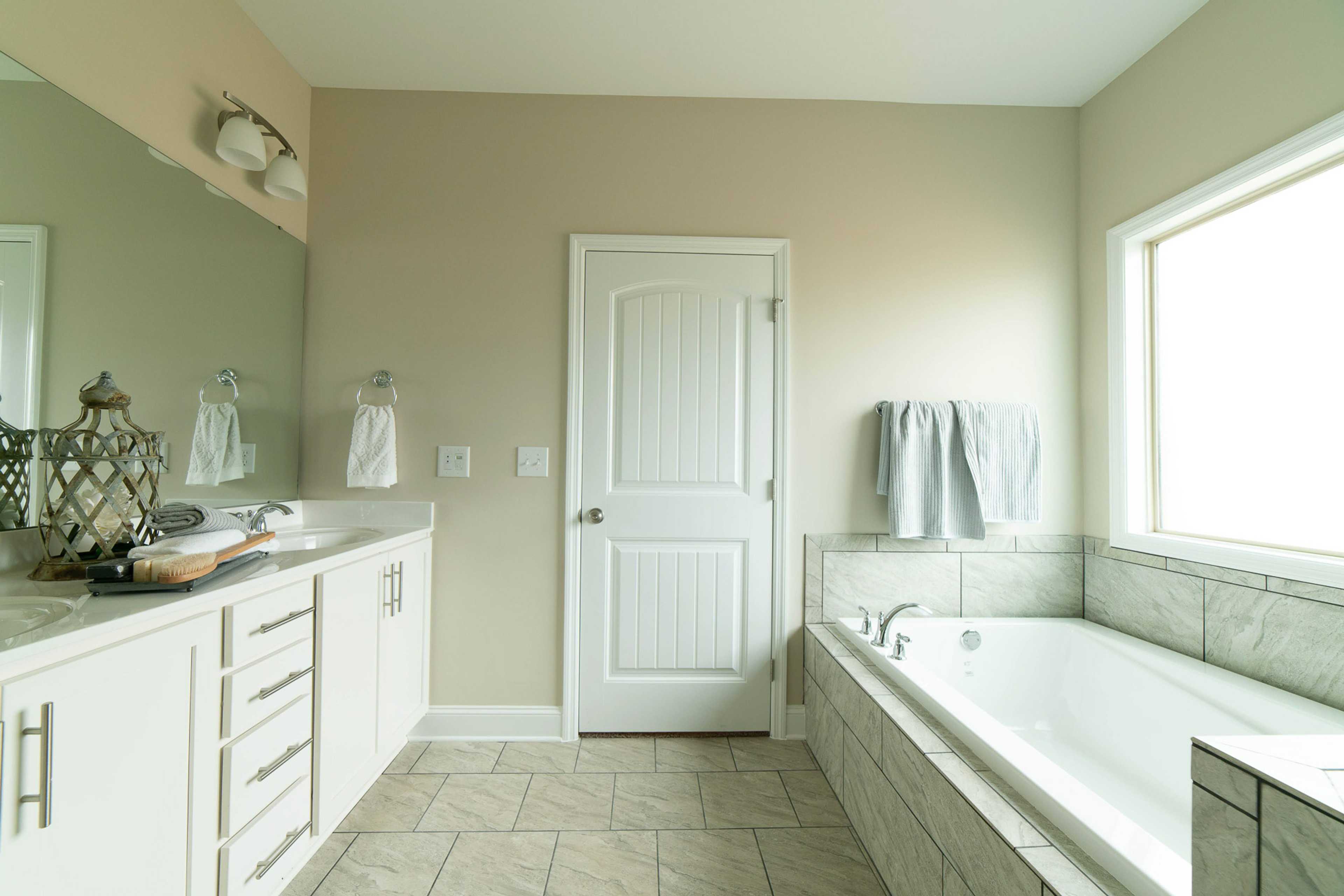 Spacious primary bathroom at The Dairy at Oak Grove in South Huntsville AL with white double vanity, soaking tub, and beige tiled walls