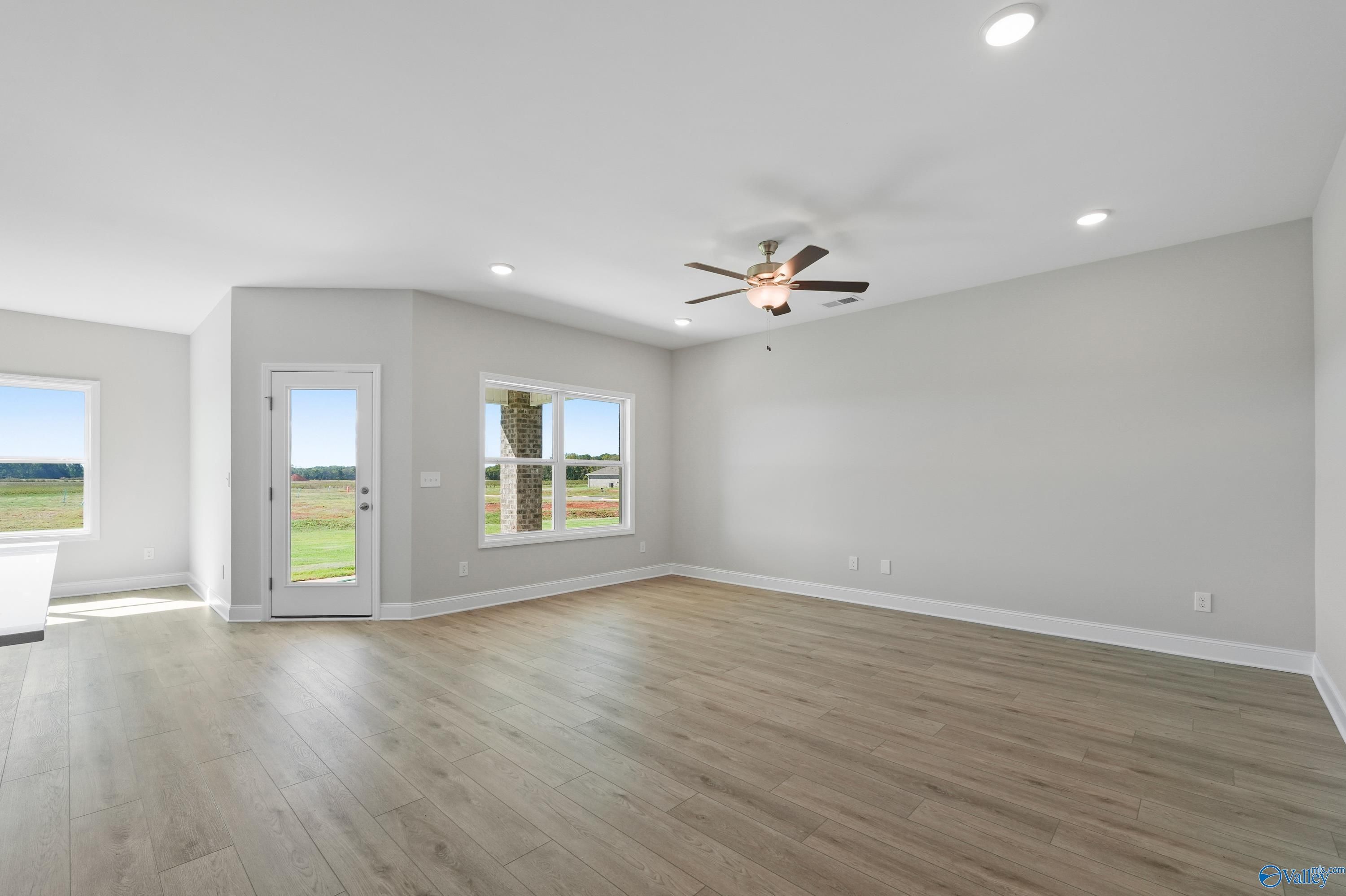 Spacious living room with hardwood floors, ceiling fan, and large windows overlooking green fields in Davidson Homes The Everett, Hazel Green, Alabama