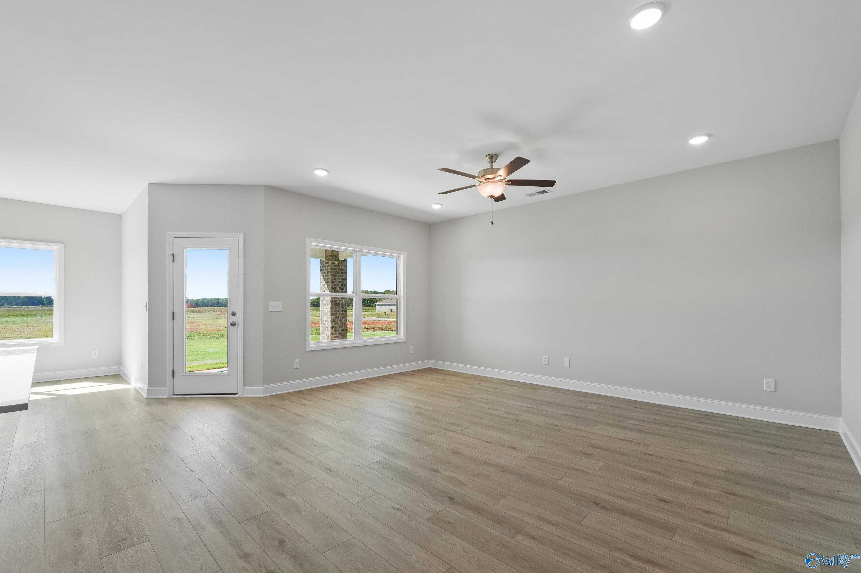 Spacious living room with hardwood floors, ceiling fan, and large windows overlooking green fields in Davidson Homes The Everett, Hazel Green, Alabama