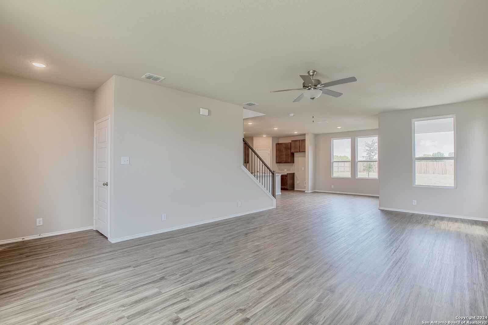 Spacious open living area with light hardwood floors, ceiling fan, staircase, and large windows in Davidson Homes The Murray H, Seguin, Texas