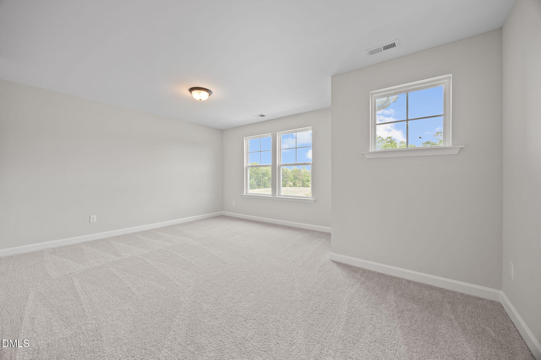 Bright empty bedroom with light gray walls, beige carpet, and large windows overlooking trees in Davidson Homes The Willow D, Wendell, NC