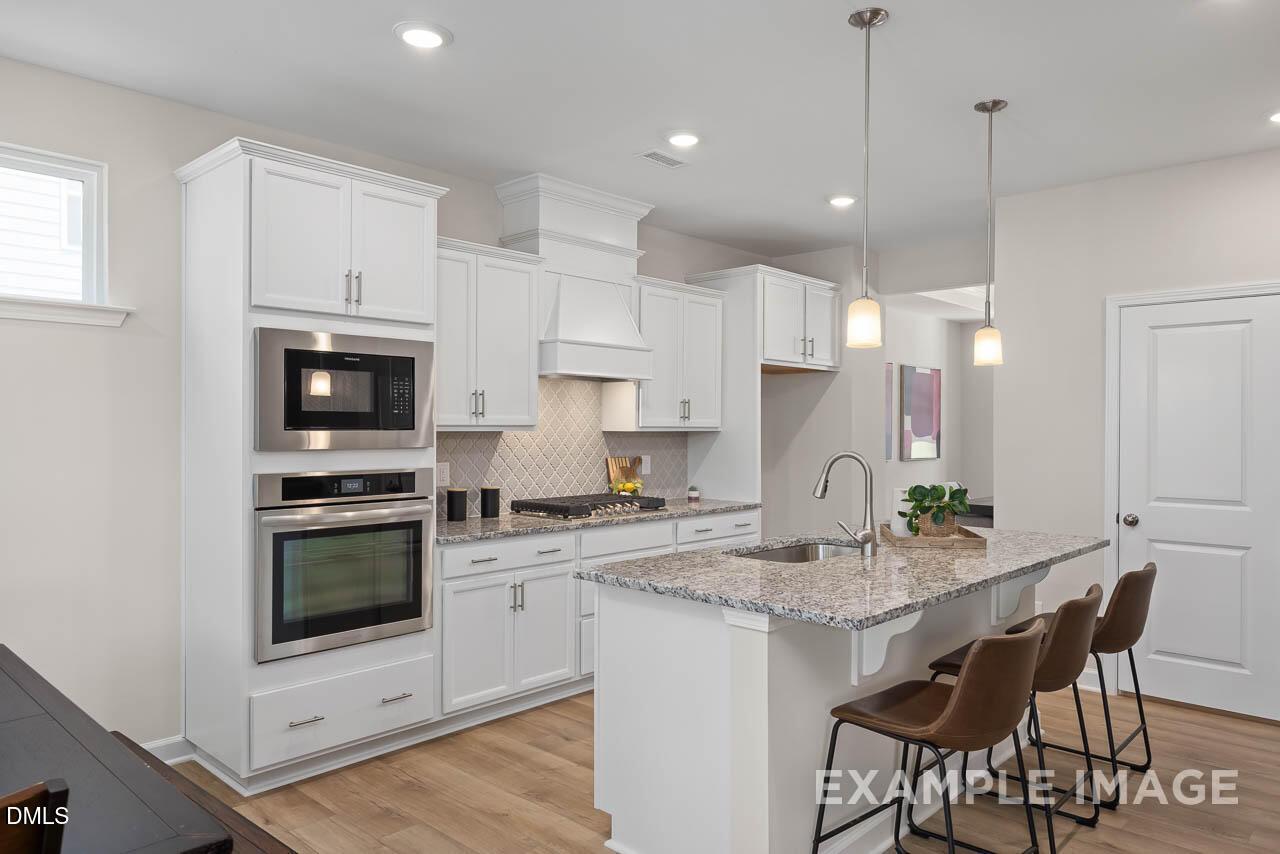 Modern white kitchen featuring granite countertops, stainless steel double oven, gas cooktop, and island seating in Davidson Homes The Willow D, Lillington, NC